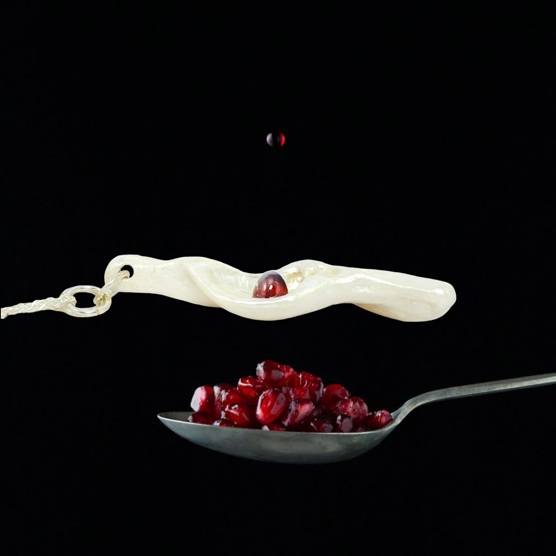 Pomegranate natural seashell pendant is adorned with a stunning Garnet gemstone. The pendant is shown over a spoonful of pomegranate seeds to show the view the colour of the gemstone.