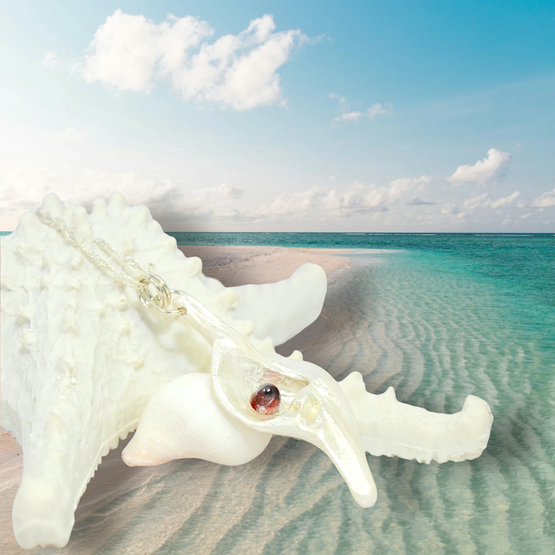 Pomegranate natural seashell pendant is adorned with a stunning Garnet gemstone. The pendant is resting on a starfish with the ocean in the background.
