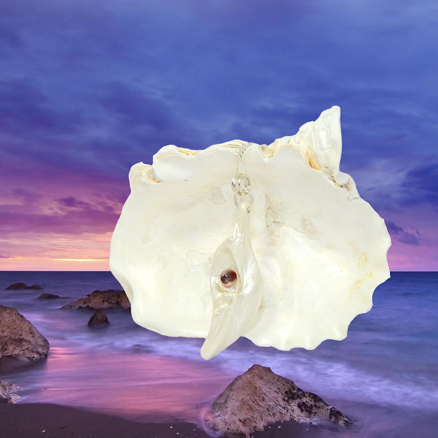 Pomegranate natural seashell pendant is adorned with a stunning Garnet gemstone. the pendant is in front of a larger seashell with a beautiful sunset over the ocean in the background.