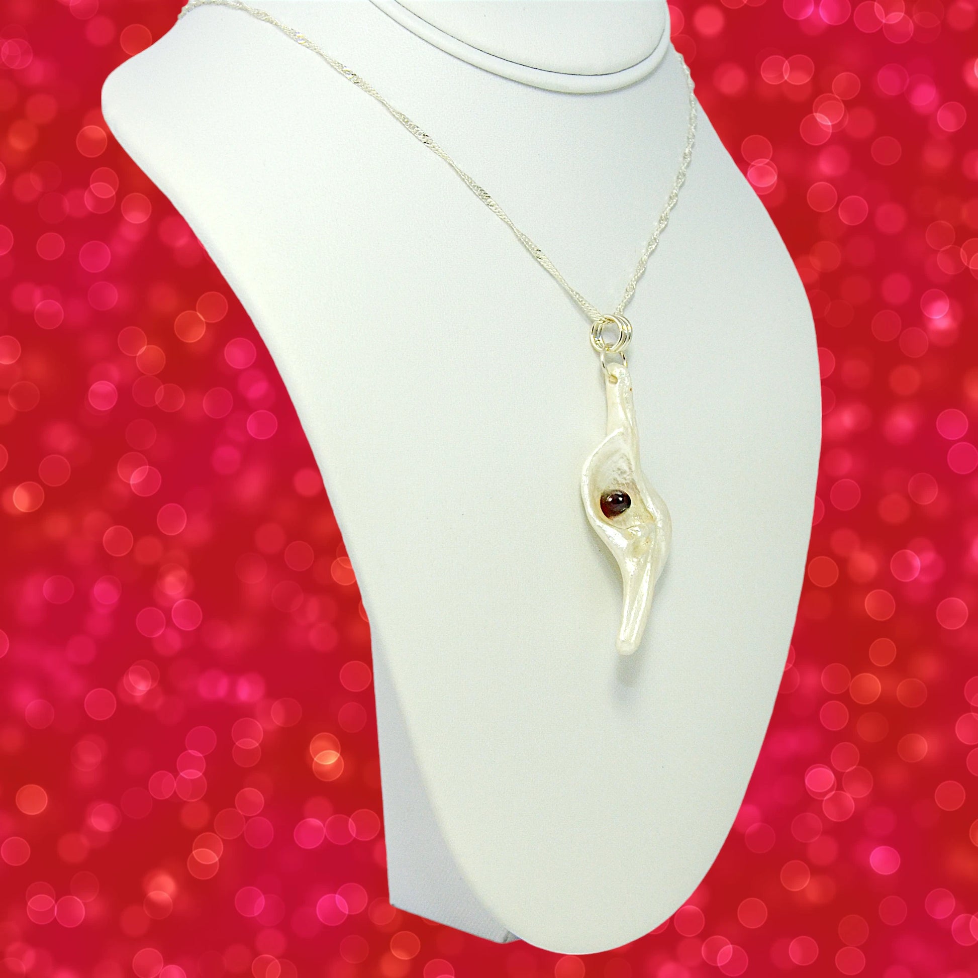 Pomegranate natural seashell pendant is adorned with a stunning Garnet gemstone. The pendant is turned so the viewer can see the right side of the pendant.