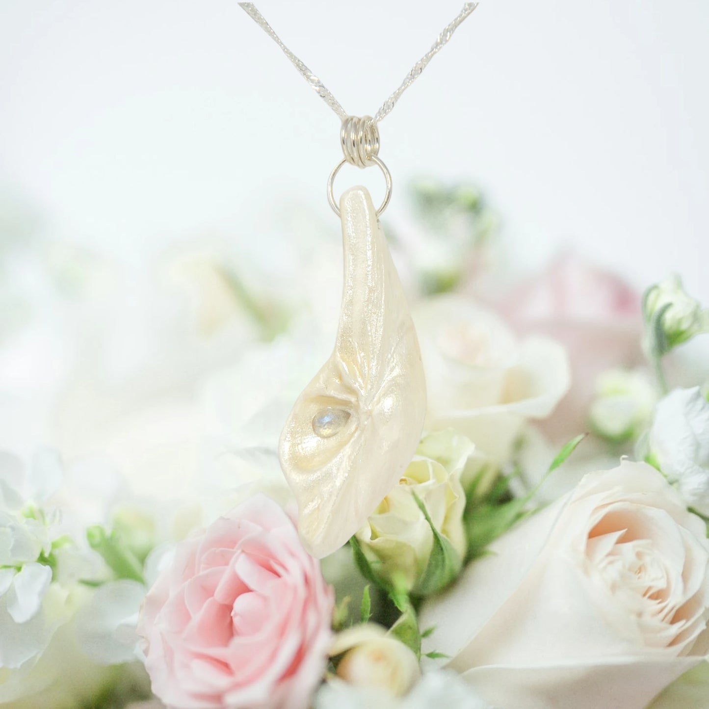 Cool Summer pendant made of natural seashell with a tear drop shape rose cut labradorite gemstone. The pendant is hanging by a chain over a bouquet of pink and white roses.