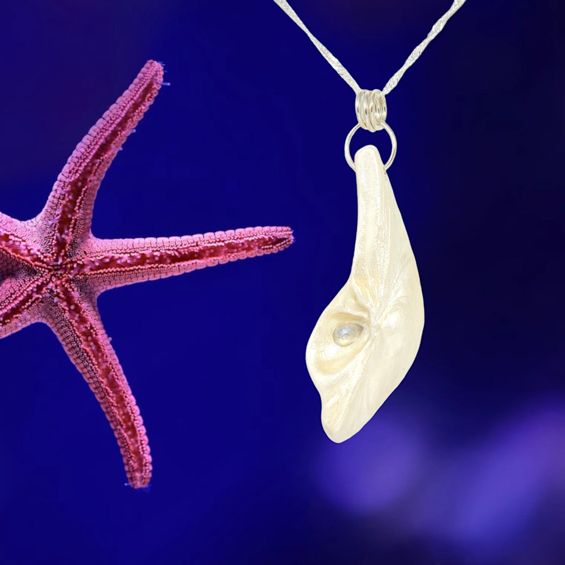 Cool Summer pendant made of natural seashell with a tear drop shape rose cut labradorite gemstone.  The pendant is shown on a blue background with a pink starfish.