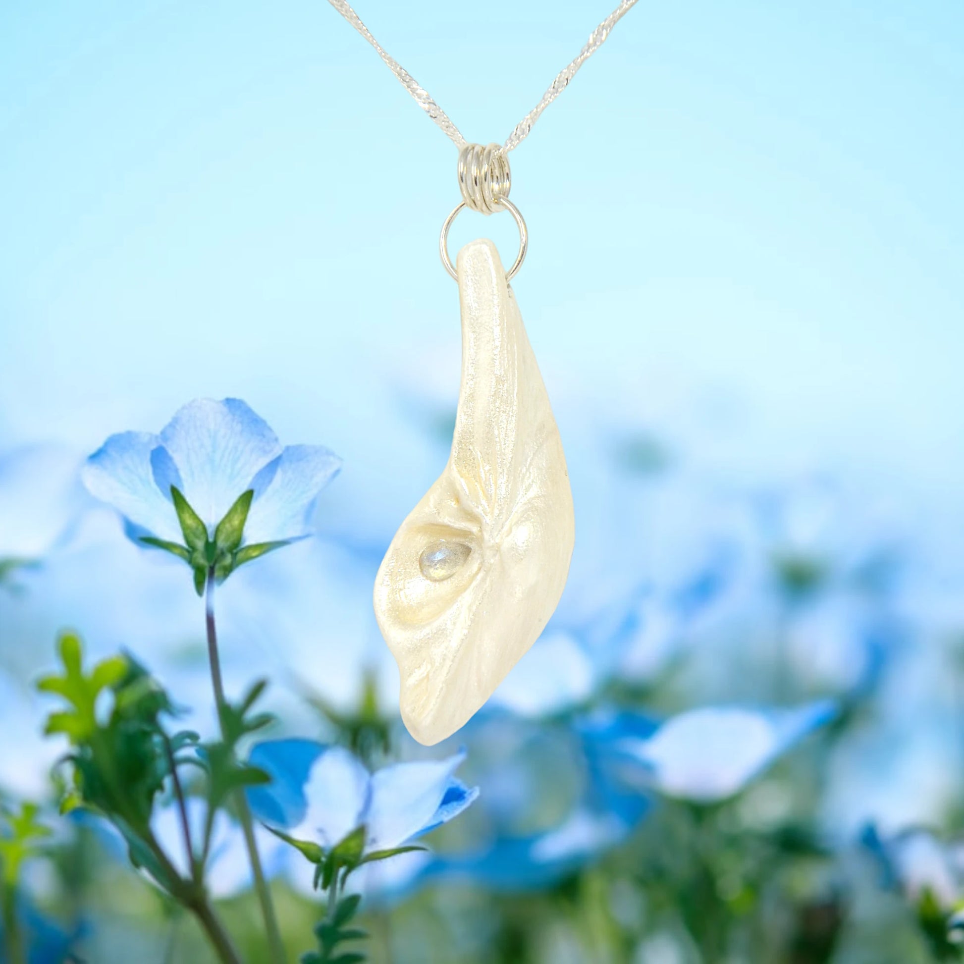 Cool Summer natural seashell pendant with tear drop shape rose cut labradorite gemstone.  Is shown hanging from a chain with a soft blue floral background.