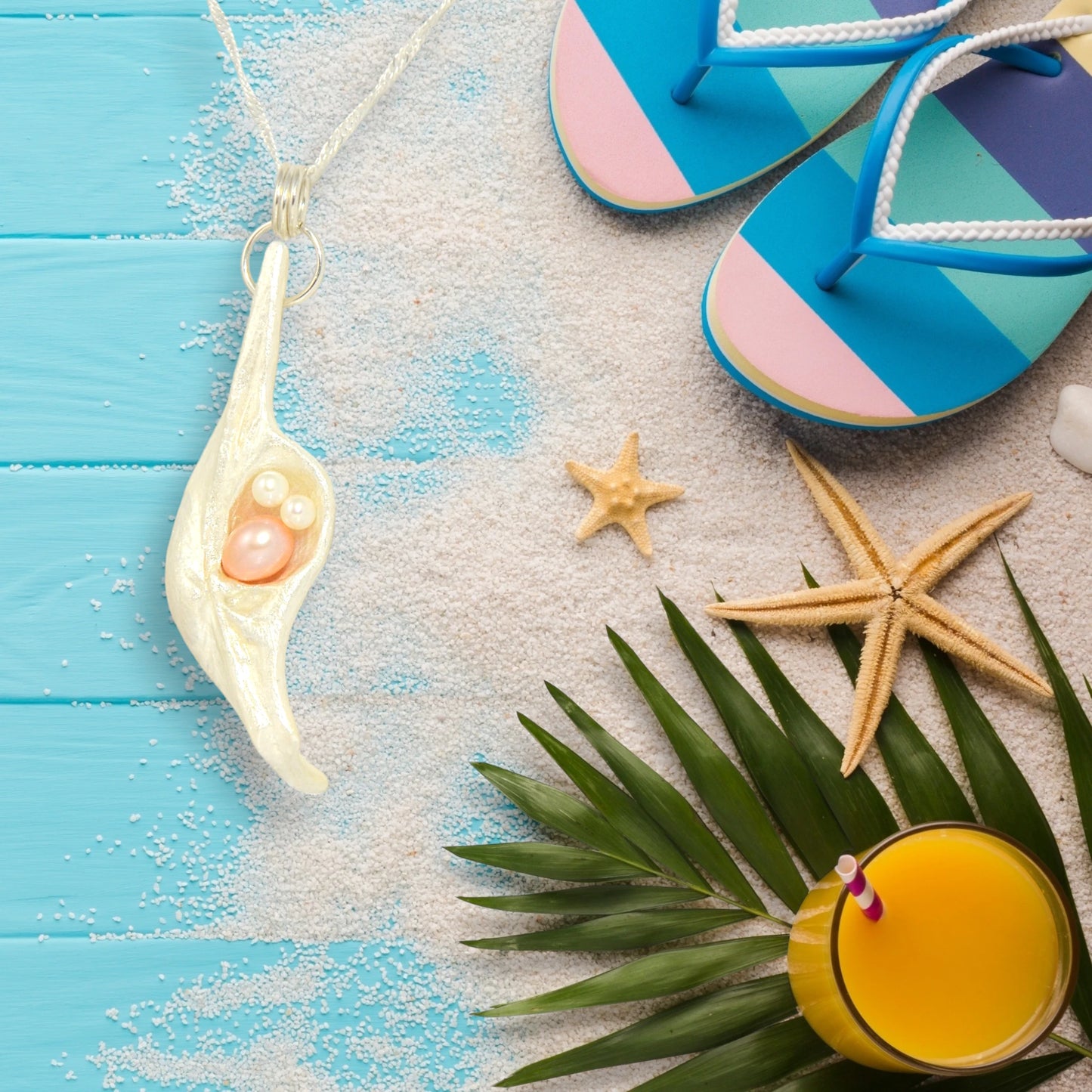 This natural seashell pendant has a real 7-8mm pink freshwater pearl and two baby pearls. The pendant is shown on a turquoise deck with sandals, starfish and a cold orange drink.