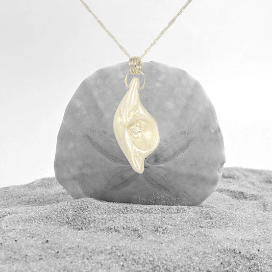 Halo natural seashell pendant with three herkimer diamonds. The pendant is shown hanging in front of a sand dollar set in sand.