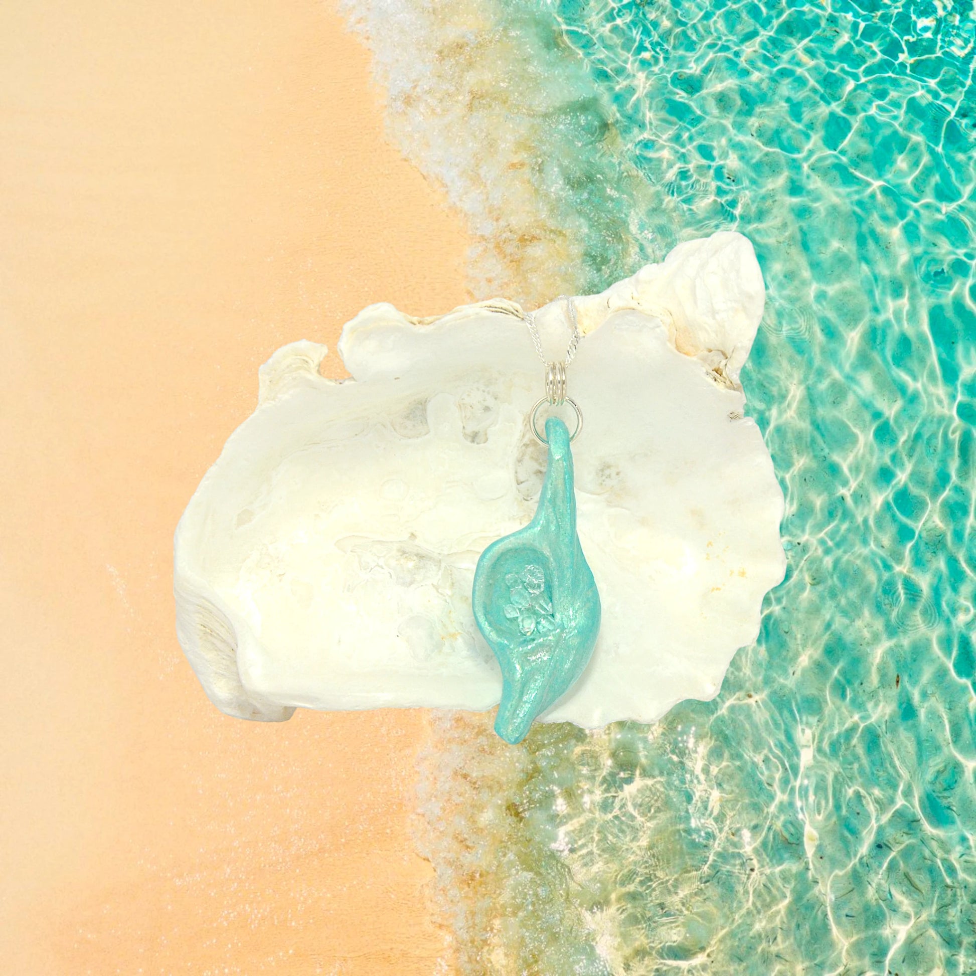 Diamond Mine Pendant is named for the eight herkimer diamonds that enhance the beauty of this gorgeous pendant! The pendant is shown hanging in front of a larger seashell.  The background is of the ocean and the waves hitting the beach.