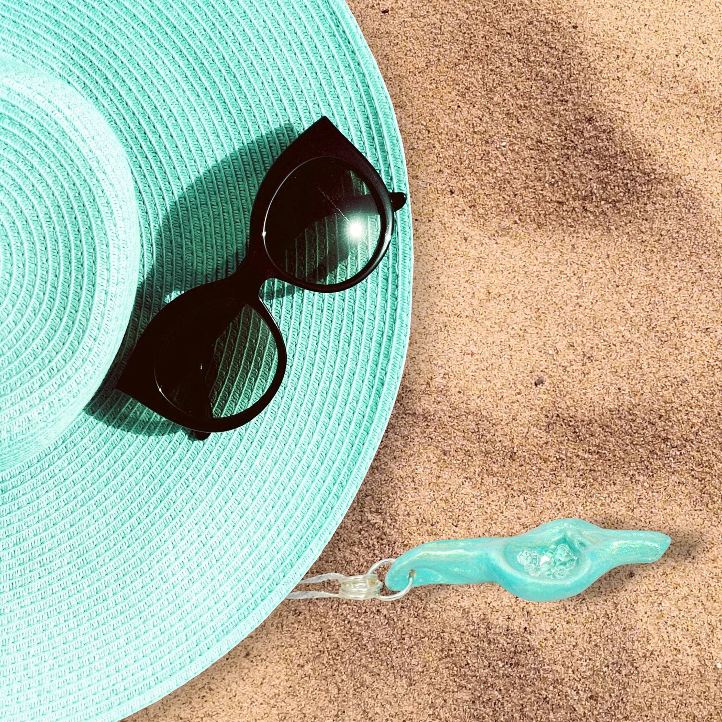 Diamond Mine Pendant is named for the eight herkimer diamonds that enhance the beauty of this gorgeous pendant! The pendant is shown laying on the sandy beach with a turquoise beach hat and black sunglasses.