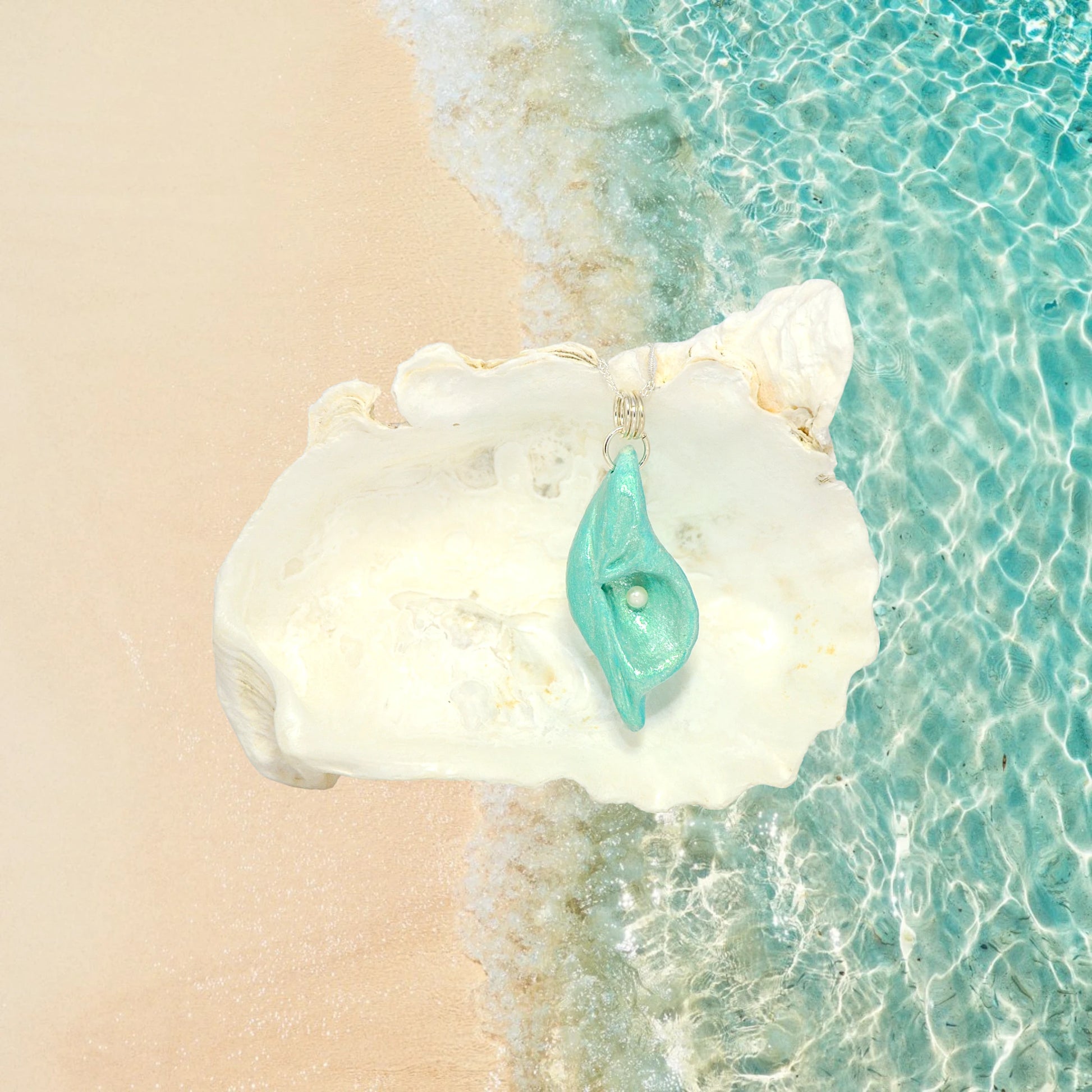 Ocean Pearl natural seashell pendant has a  real freshwater baby pearl. The pendant is shown in front of a larger seashell.  The beach and the ocean meet in the background.