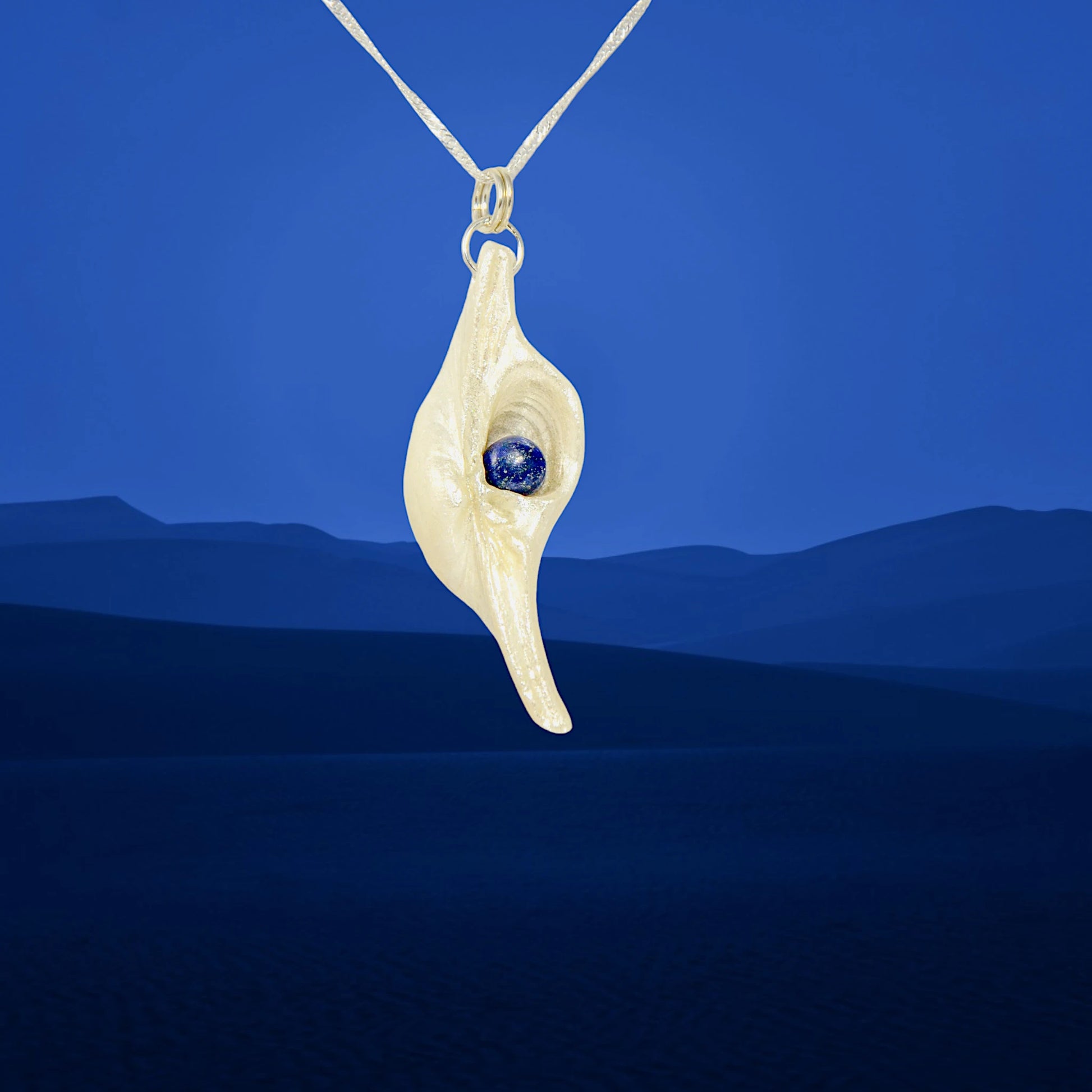 Vision is a natural seashell pendant with a Lapis Lazuli gemstone.  A blue mountain background.