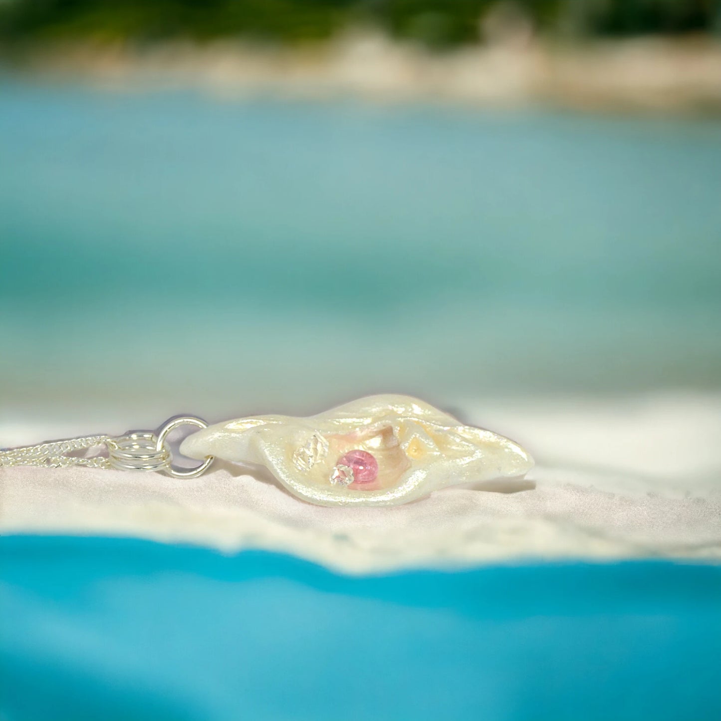 This natural seashell pendant has Pink Tourmaline gemstone and three Herkimer Diamonds that compliments the pendant. The background shows the pendant on the beach.