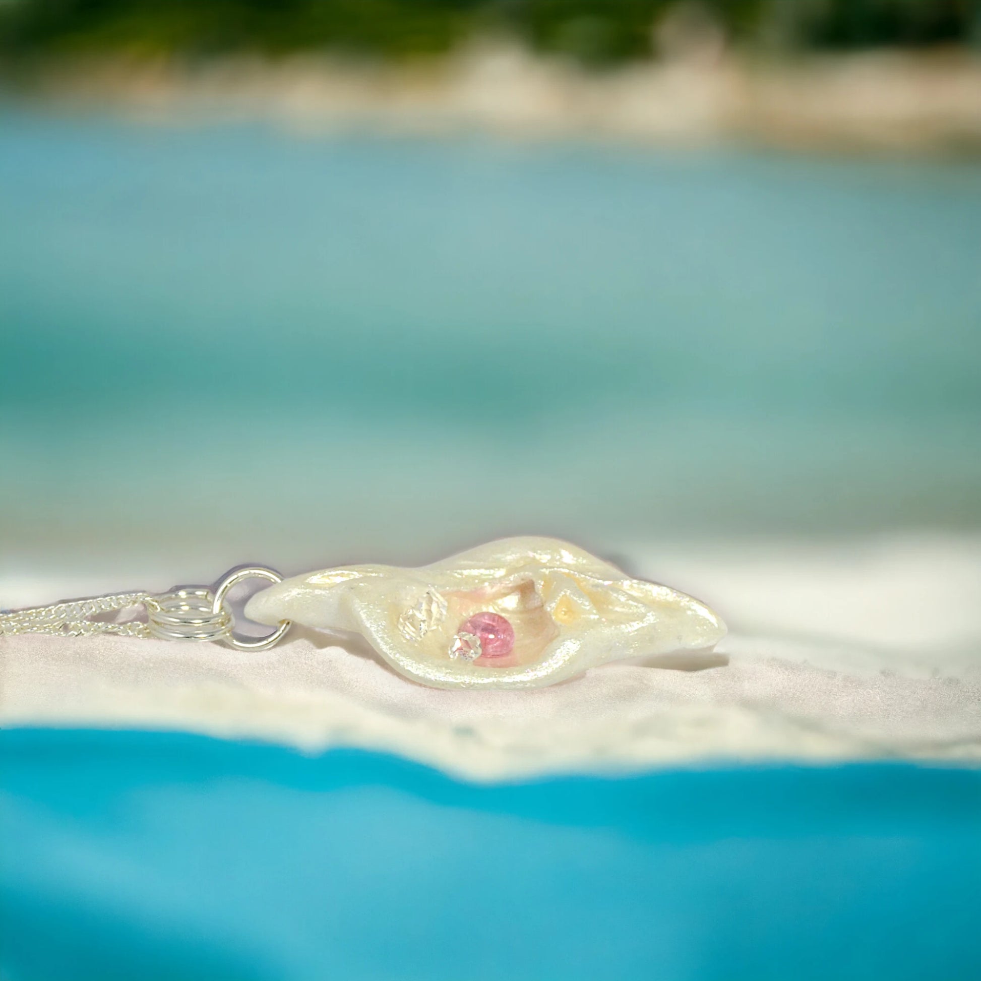 This natural seashell pendant has Pink Tourmaline gemstone and three Herkimer Diamonds that compliments the pendant. The background shows the pendant on the beach.
