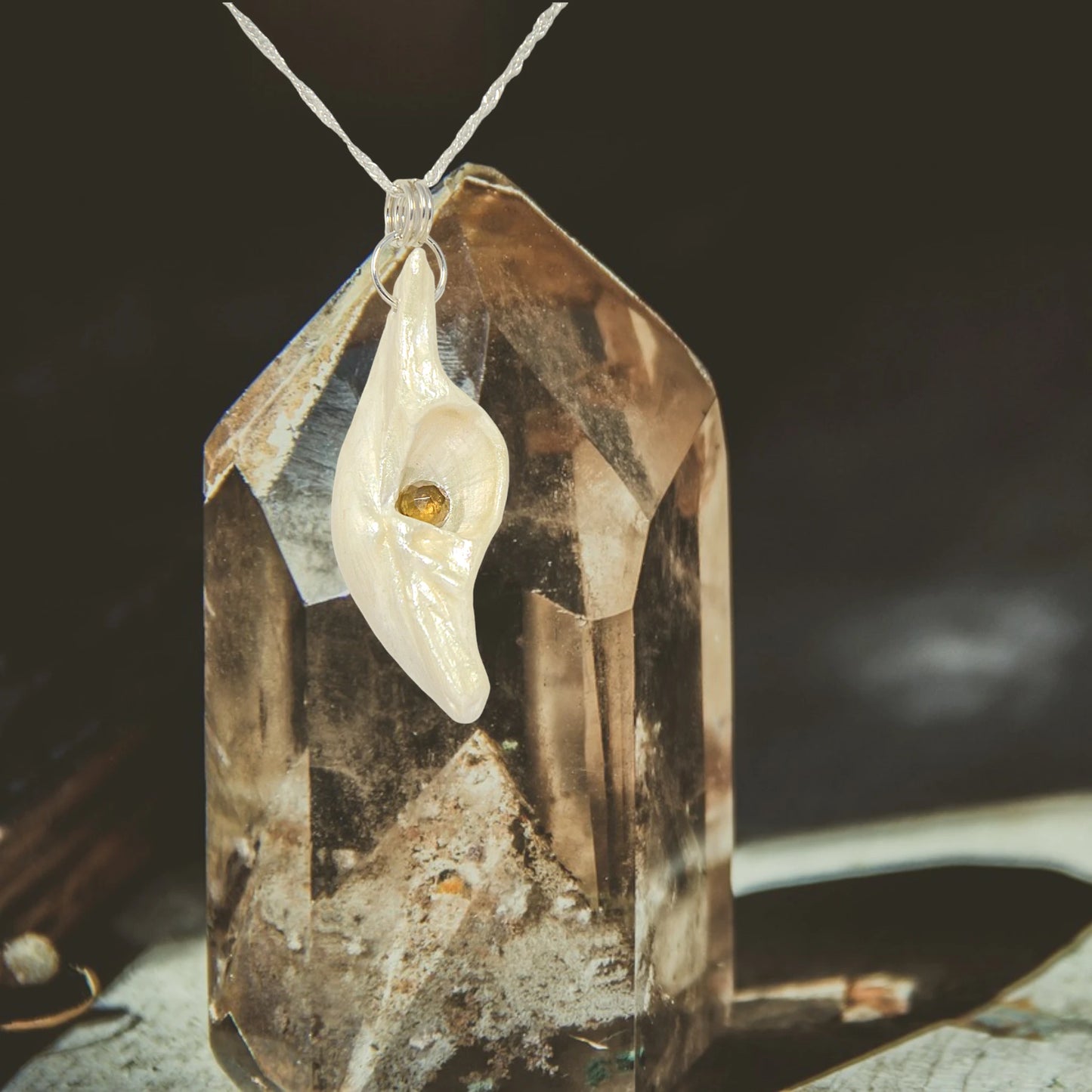 Seer is a natural seashell pendant with a beautiful 5mm rose cut Smokey Quartz compliments the pendant. The pendant is shown in front of a larger piece of smoky quartz.