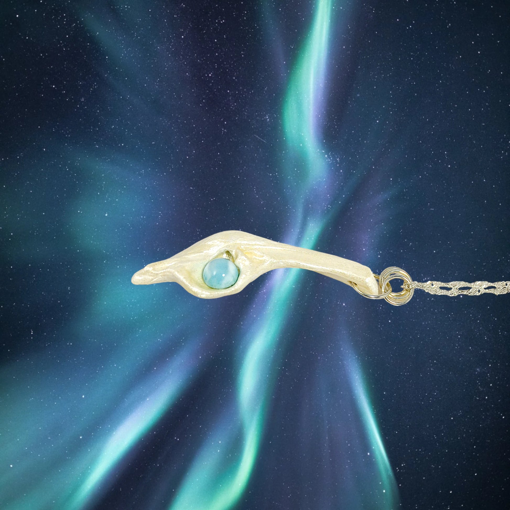 Larimar Moon Natural seashell a beautiful 10 mm Round Larimar Gemstone compliments the pendant. The pendant is shown on a white necklace displayer with the northern lights in the background.