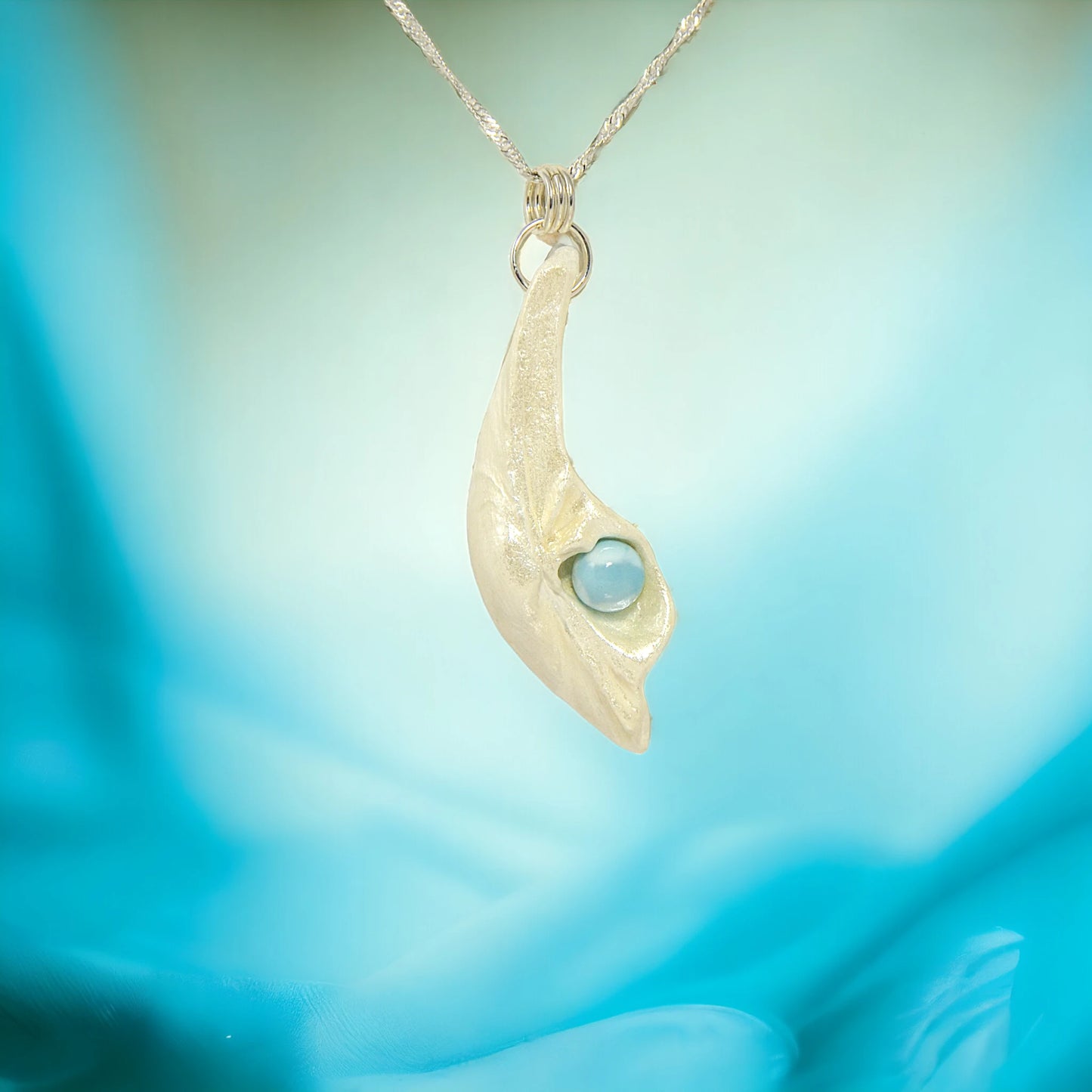 Larimar Moon Natural seashell a beautiful 10 mm Round Larimar Gemstone compliments the pendant. The pendant is shown on a white necklace displayer with a blue background.