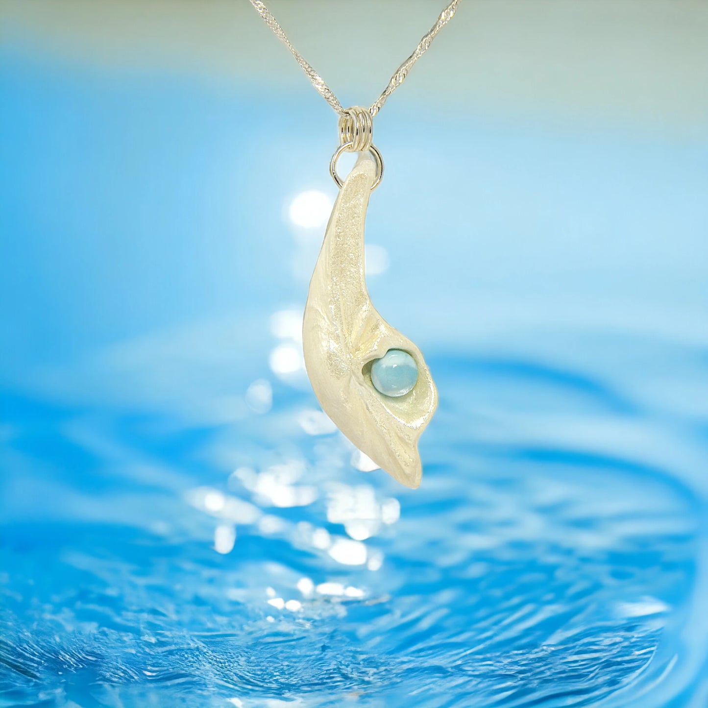 Larimar Moon Natural seashell a beautiful 10 mm Round Larimar Gemstone compliments the pendant. The pendant is shown hanging over a sunlight body of water.