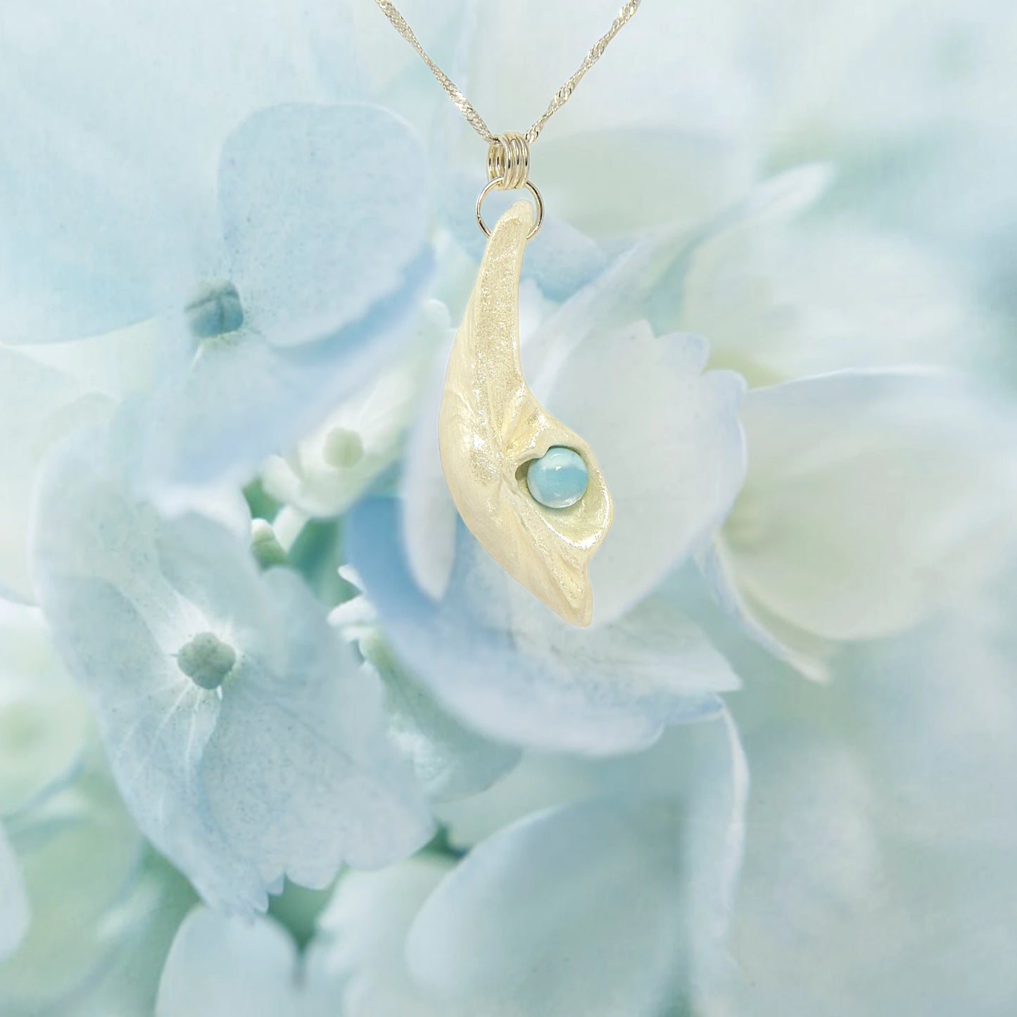 Larimar Moon Natural seashell a beautiful 10 mm Round Larimar Gemstone compliments the pendant. The pendant is shown on a bed of soft blue flowers.