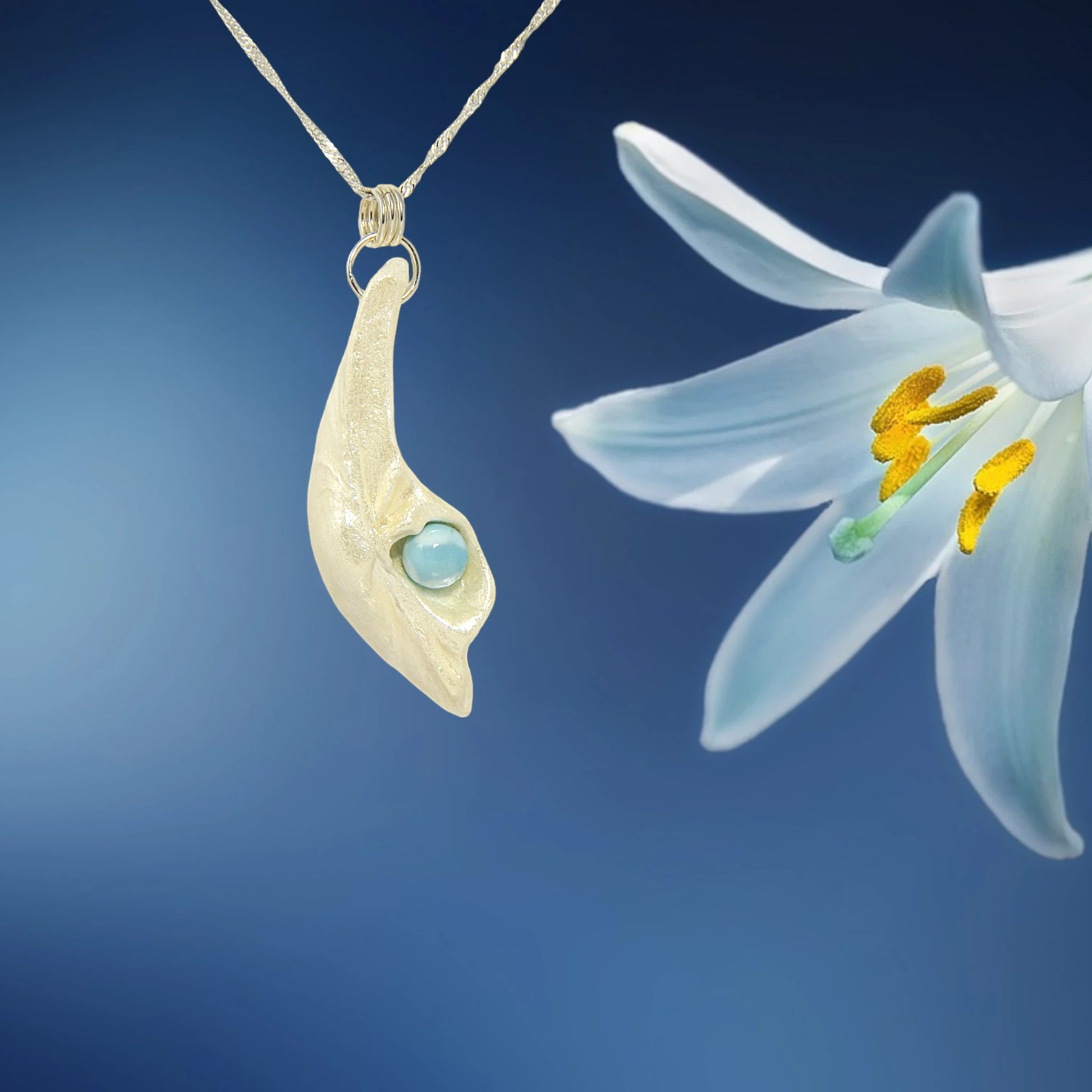 Larimar Moon Natural seashell a beautiful 10 mm Round Larimar Gemstone compliments the pendant. The pendant is shown on a white necklace displayer with white lily flower and a blue background.