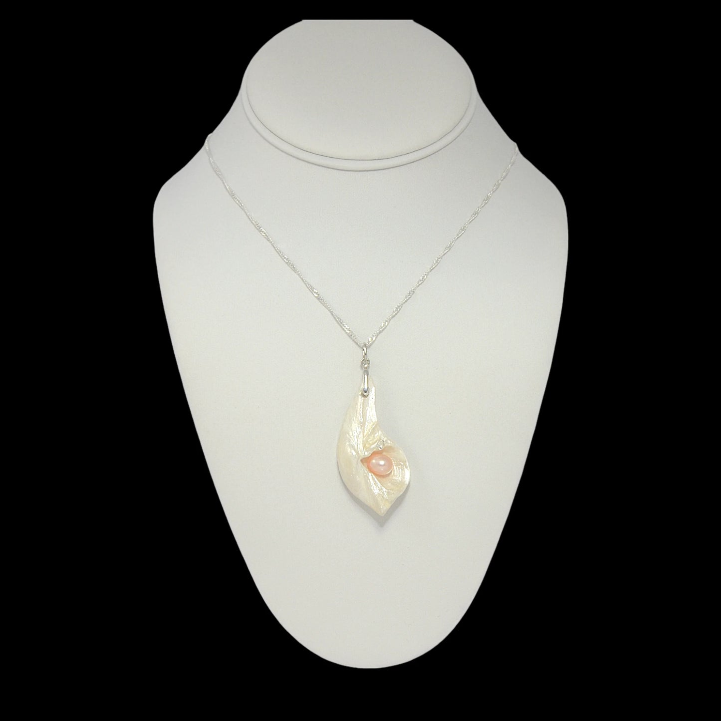 Athena is the name of the pendant being showcased.  It is a natural seashell from the beaches of Vancouver Island. The pendant has a real pink freshwater pearl and a faceted herkimer diamond. It is being showcased with a necklace on a neck displayer.