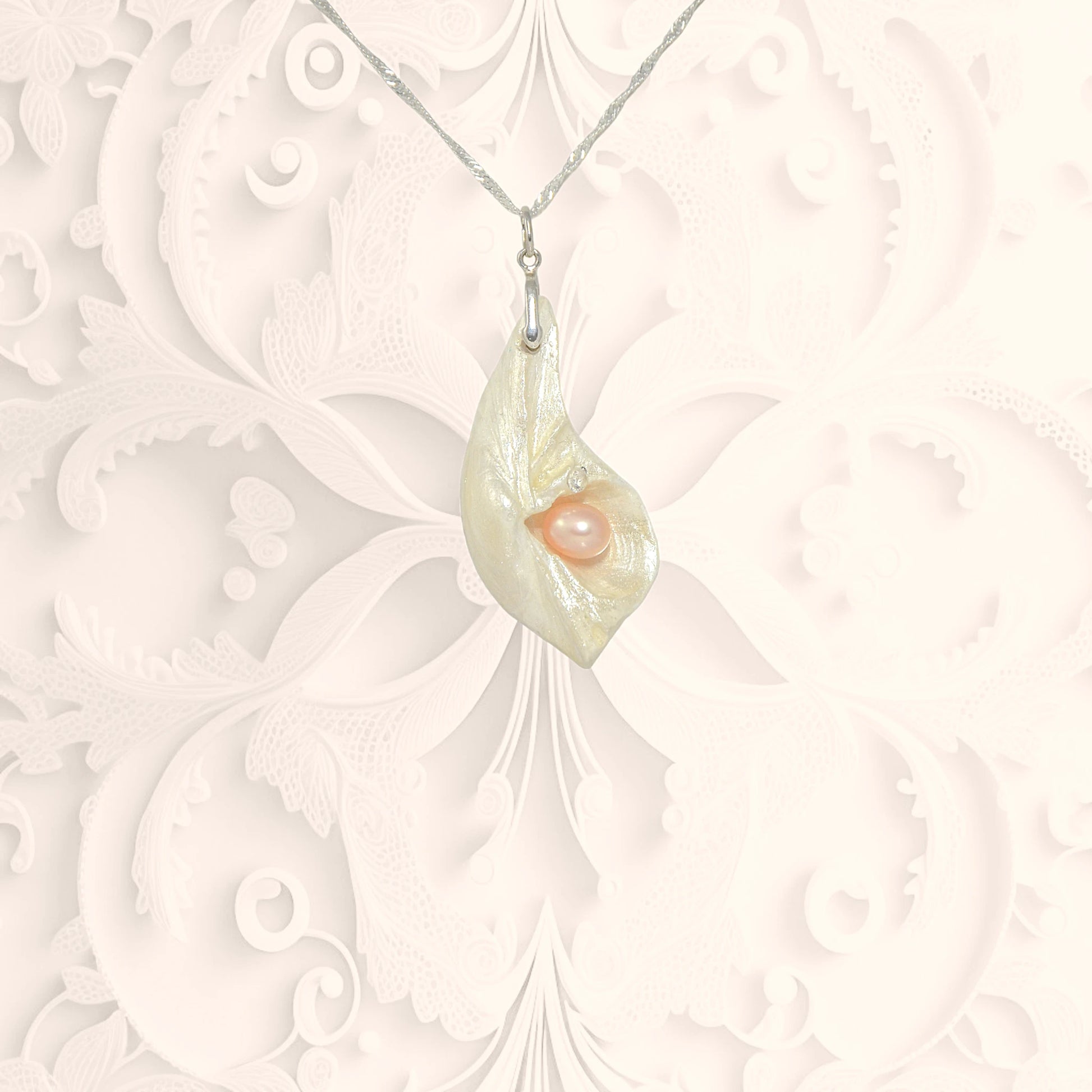 Athena is the name of the pendant in front of a white ornate background..  It is a natural seashell from the beaches of Vancouver Island. The pendant has a real pink freshwater pearl and a faceted herkimer diamond. 