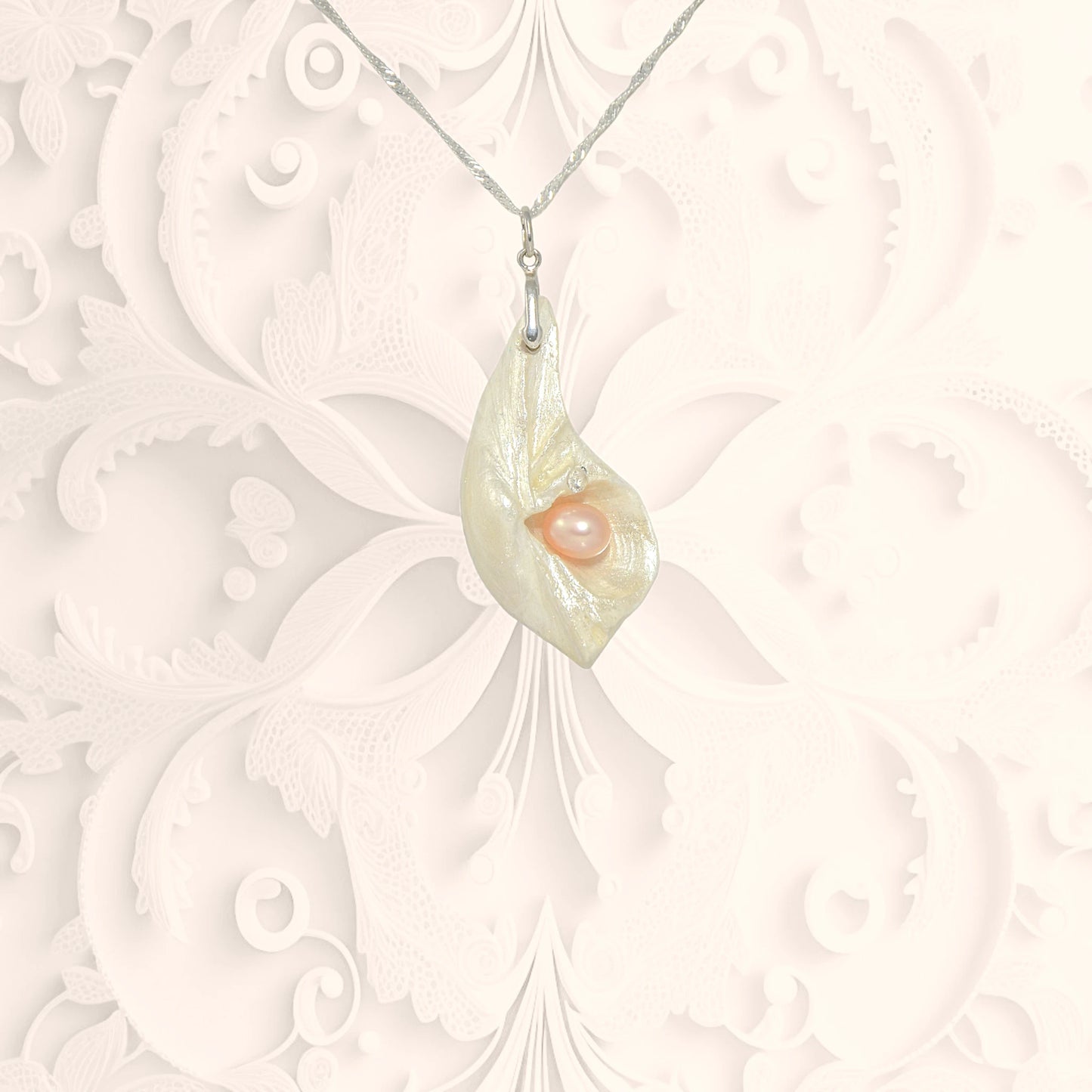 Athena is the name of the pendant in front of a white ornate background..  It is a natural seashell from the beaches of Vancouver Island. The pendant has a real pink freshwater pearl and a faceted herkimer diamond. 