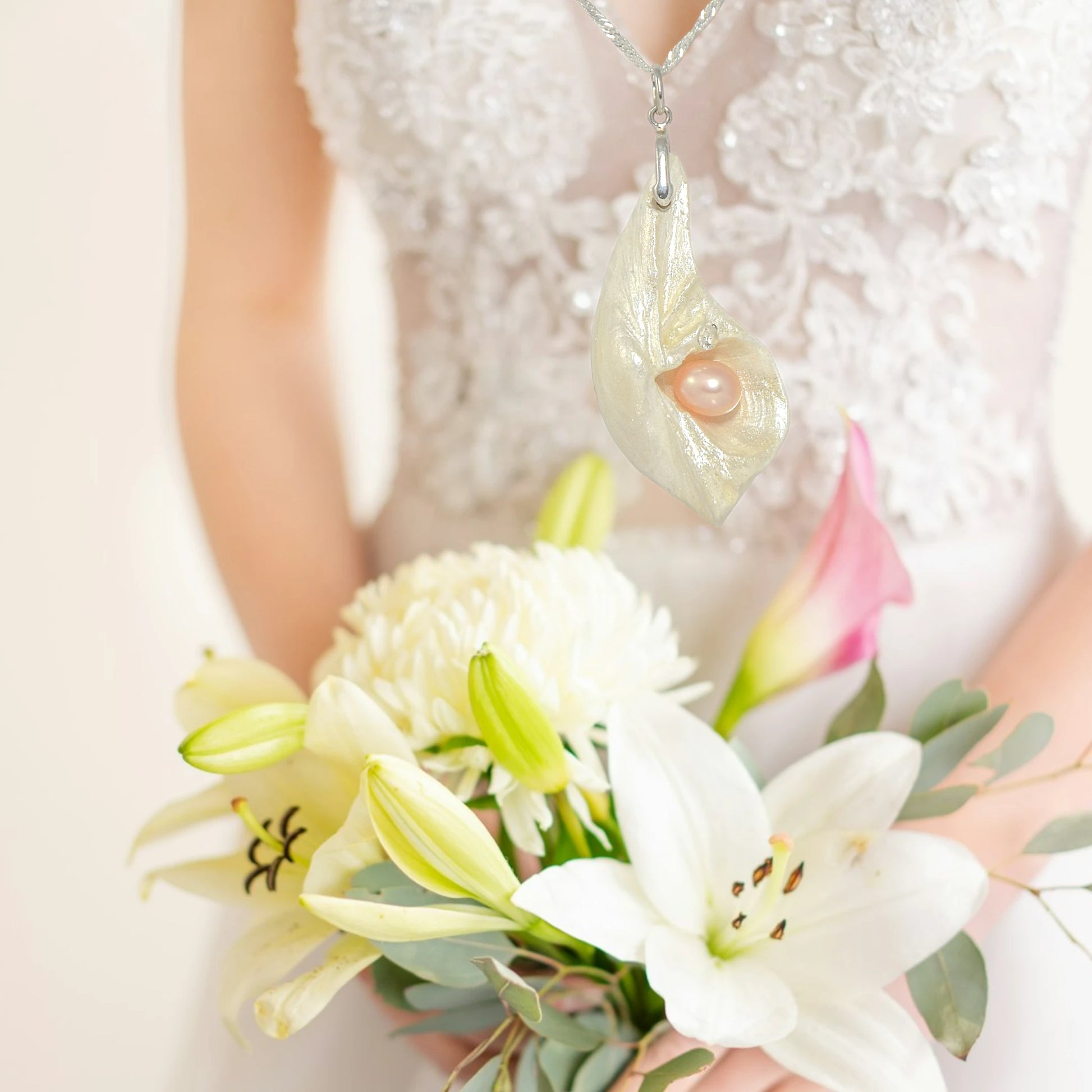 The pendant being showcased with a bride holding her bouquet..  It is a natural seashell from the beaches of Vancouver Island. The pendant has a real pink freshwater pearl and a faceted herkimer diamond. The pendant is hanging over a bouquet of pink and white flowers.