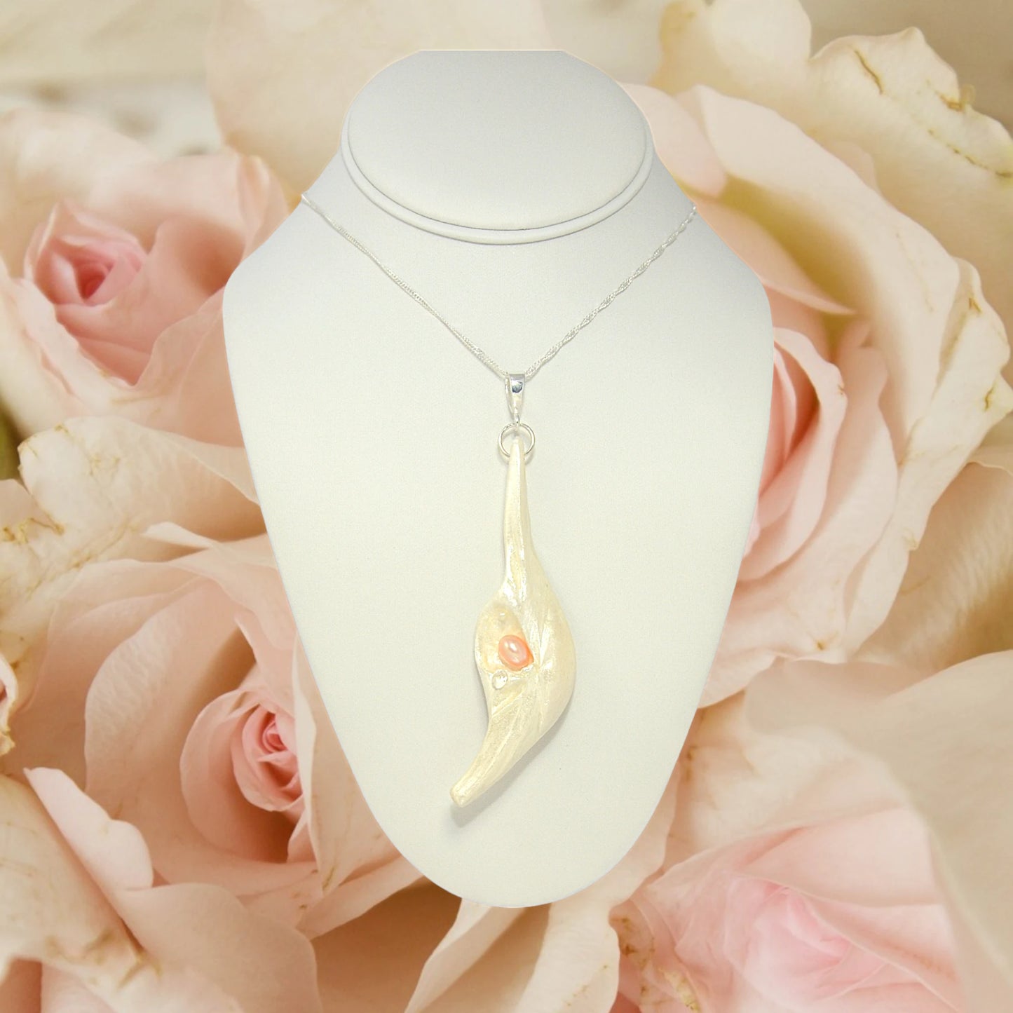 Nefertiti natural seashell and a real 8 mm pink freshwater Pearl, a baby pearl and a 5mm faceted Herkimer diamond compliments the pendant. The pendant is shown hanging a white necklace displayer with pink roses in the background.