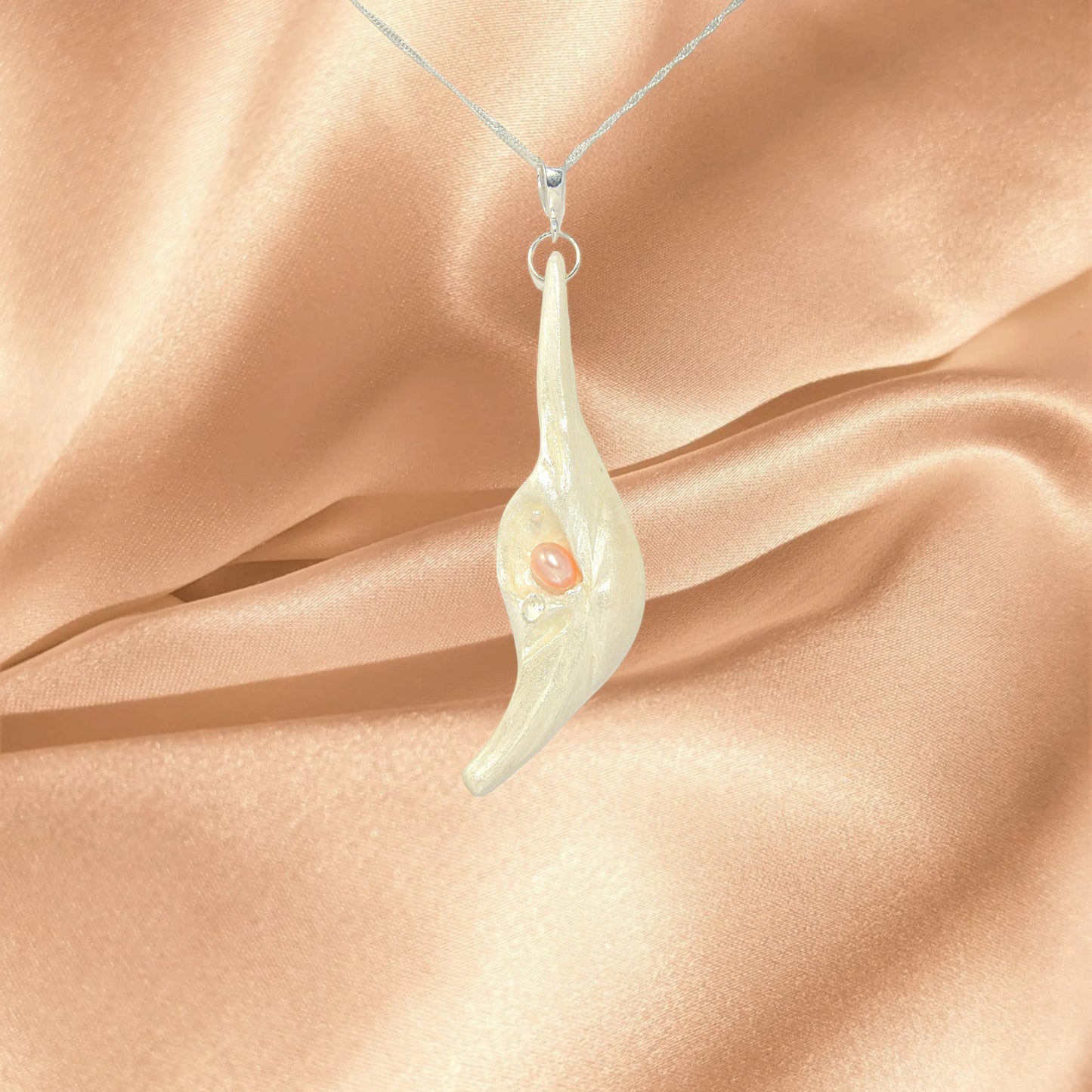 Nefertiti natural seashell and a real 8 mm pink freshwater Pearl, a baby pearl and a 5mm faceted Herkimer diamond compliments the pendant. The pendant is draped in front of a peach satin.