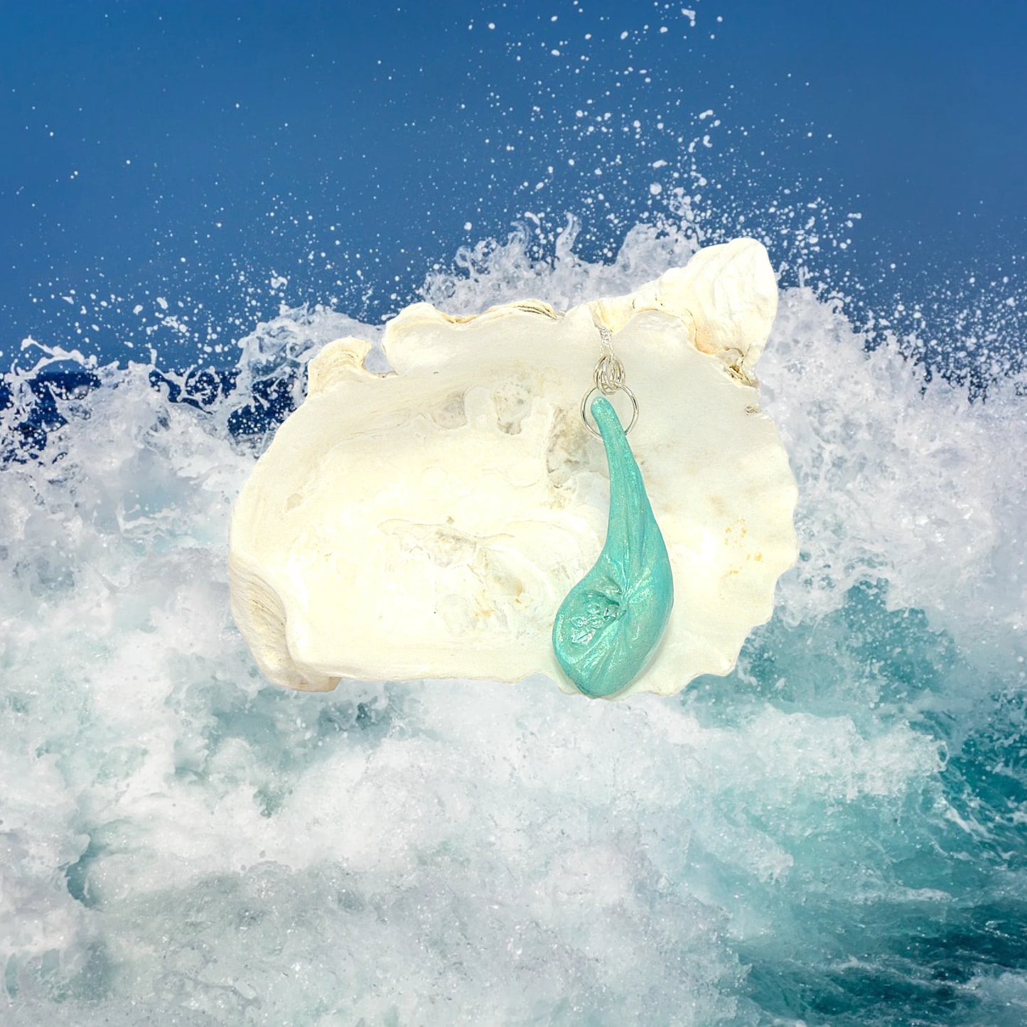 The Cascadia Pendant created with a natural seashell from the beaches of Vancouver Island.  The seashell is turquoise and has high quality herkimer diamonds. The pendant is hanging from a larger seashell with ocean waves crashing in the background.