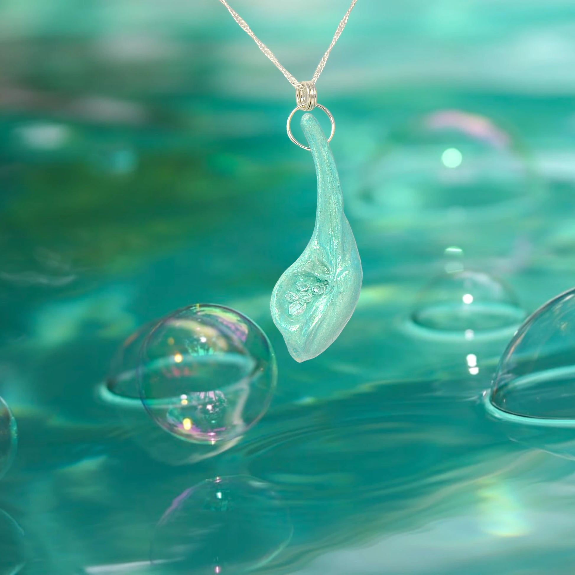 The Cascadia Pendant created with a natural seashell from the beaches of Vancouver Island.  The seashell is turquoise and has high quality herkimer diamonds. The pendant is hanging over a sea of green with bubbles near and on top of the water.