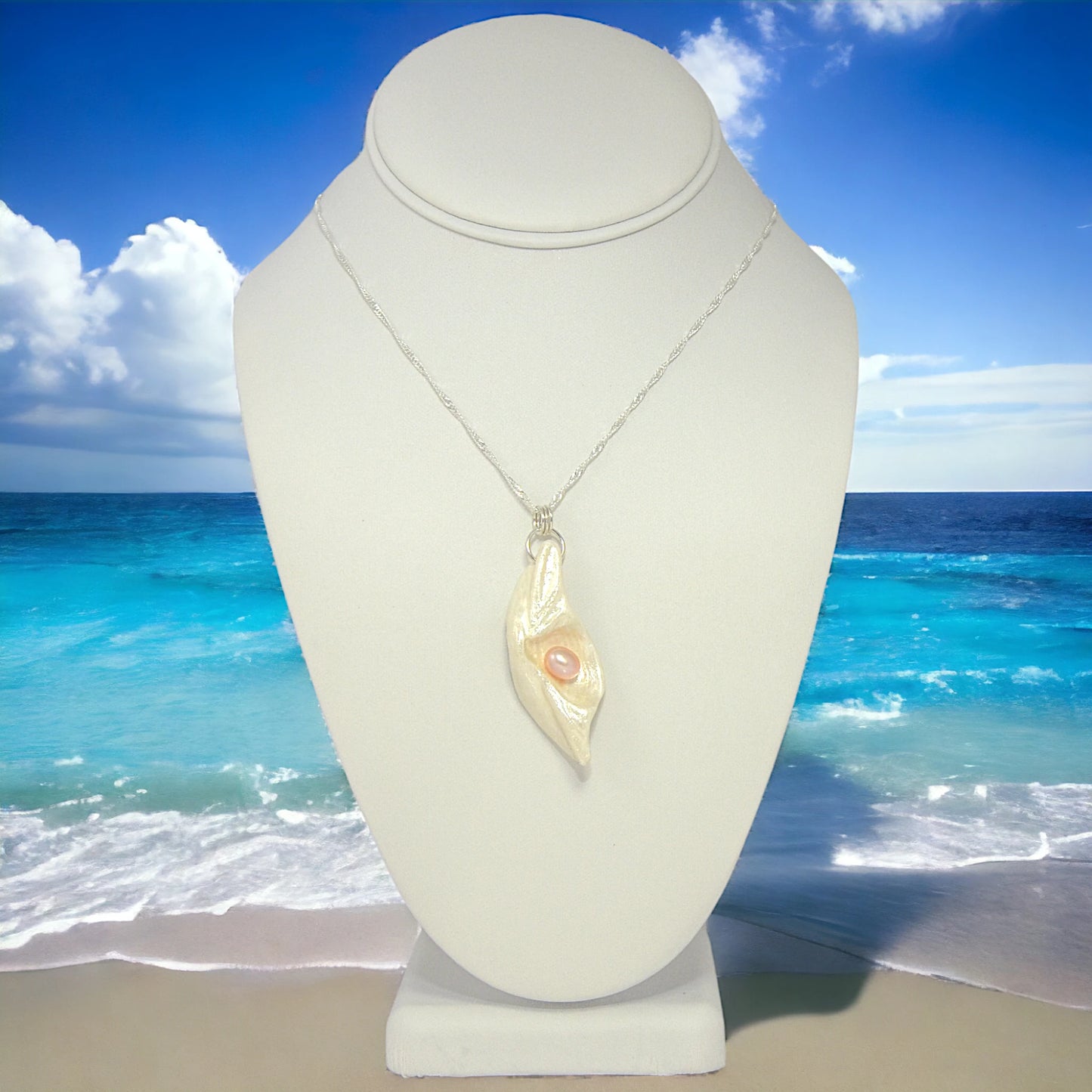 Glow natural seashell pendant with a pink freshwater pearl. The pendant is shown on a white necklace displayer with an ocean background.