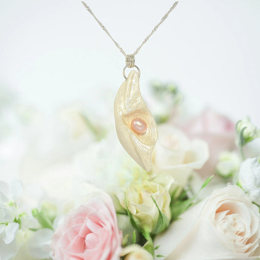 Glow natural seashell pendant with a pink freshwater pearl.  The pendant is hanging from a necklace over a bouquet of pink and white roses.