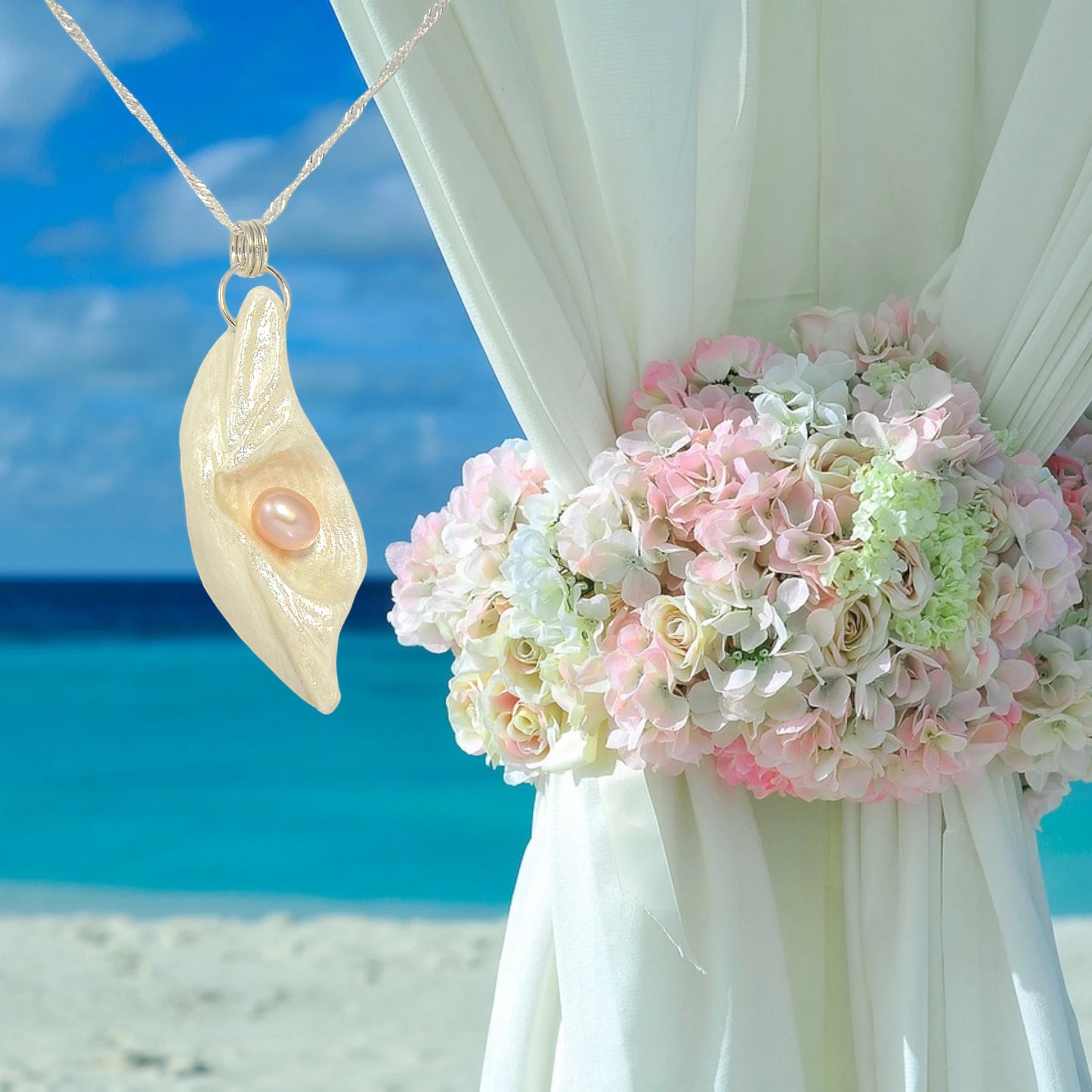 Glow natural seashell pendant with a pink freshwater pearl. The pendant hangs next to a bouquet of florals wrapped around a curtain for a beach wedding.