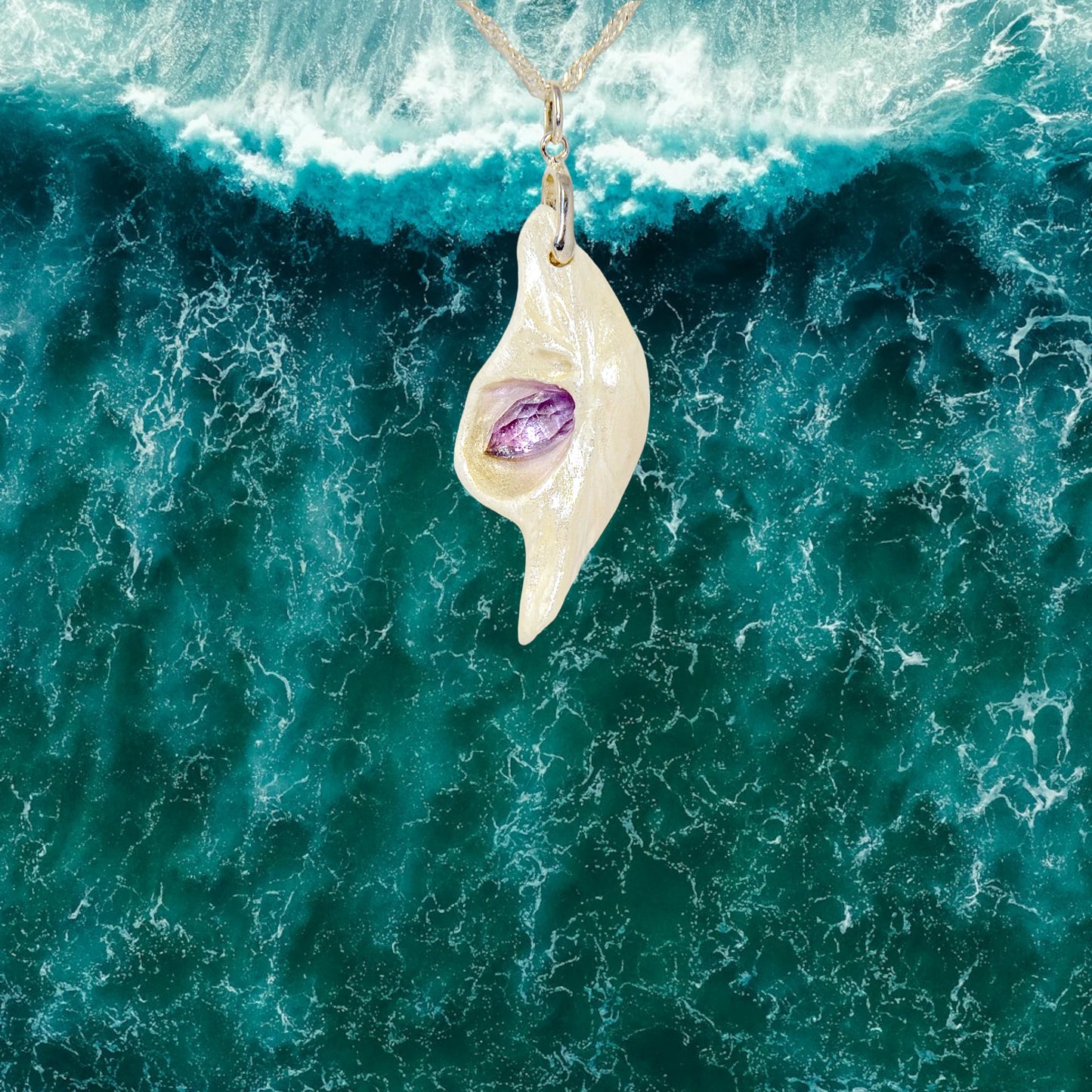 Intuition a natural seashell pendant with a beautiful rose cut marquise Amethyst.  the pendant is hanging over the ocean.