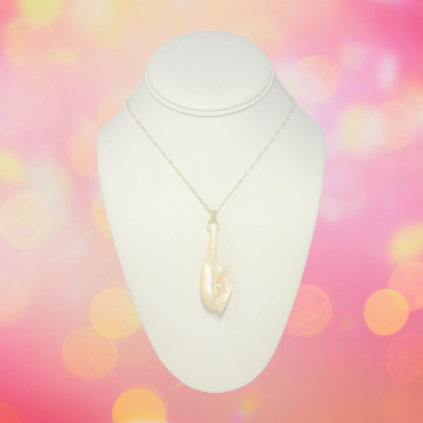 Amara is the name of this one of a kind pendant made from a natural seashell from the beach of Vancouver Island.  The pendant has a real freshwater pearl.  The pendant is being showcased on a neckline with a pink bokeh background.