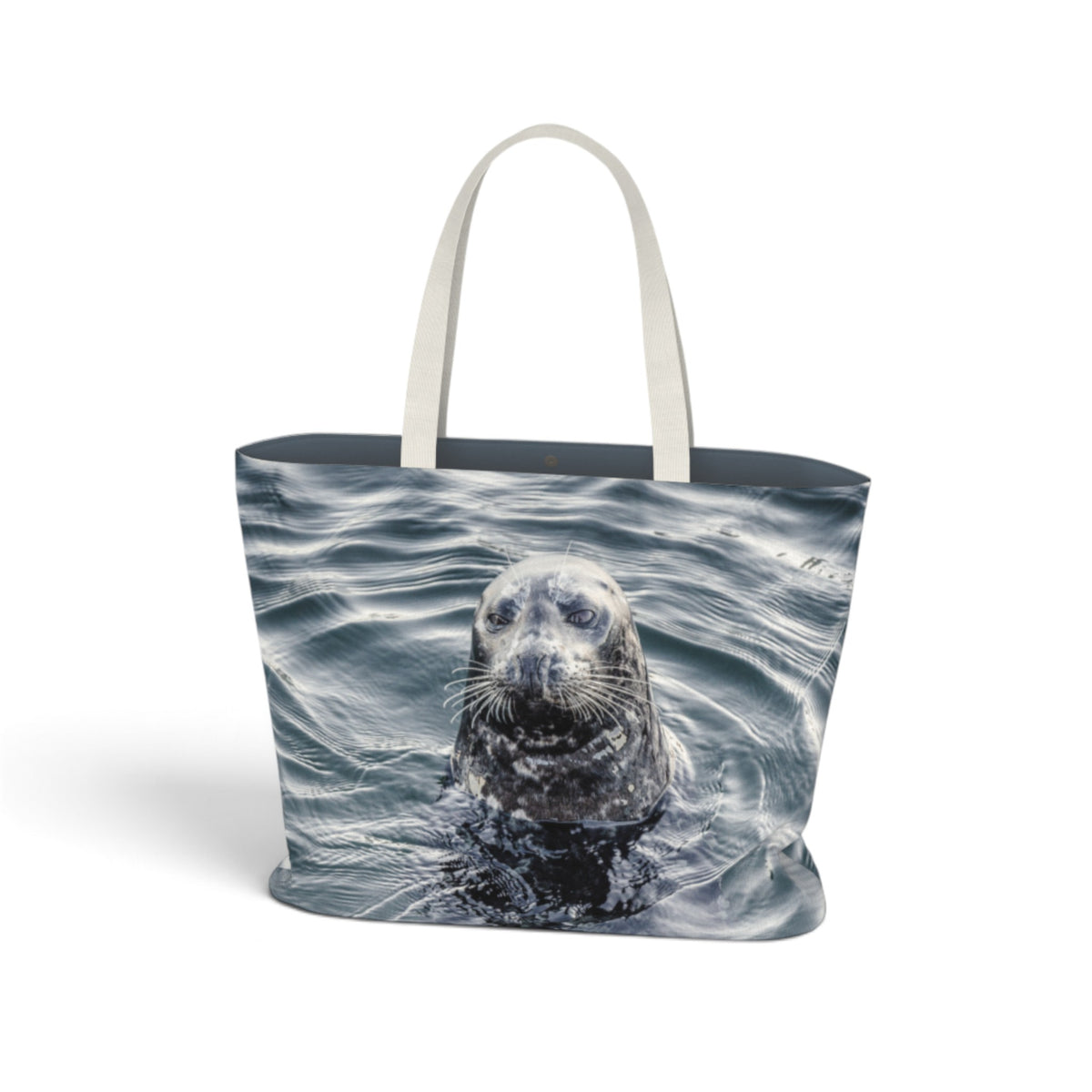 A tote bag featuring a photographic print of a seal surfacing in ocean water, with light beige fabric handles, shown against a plain white background.
