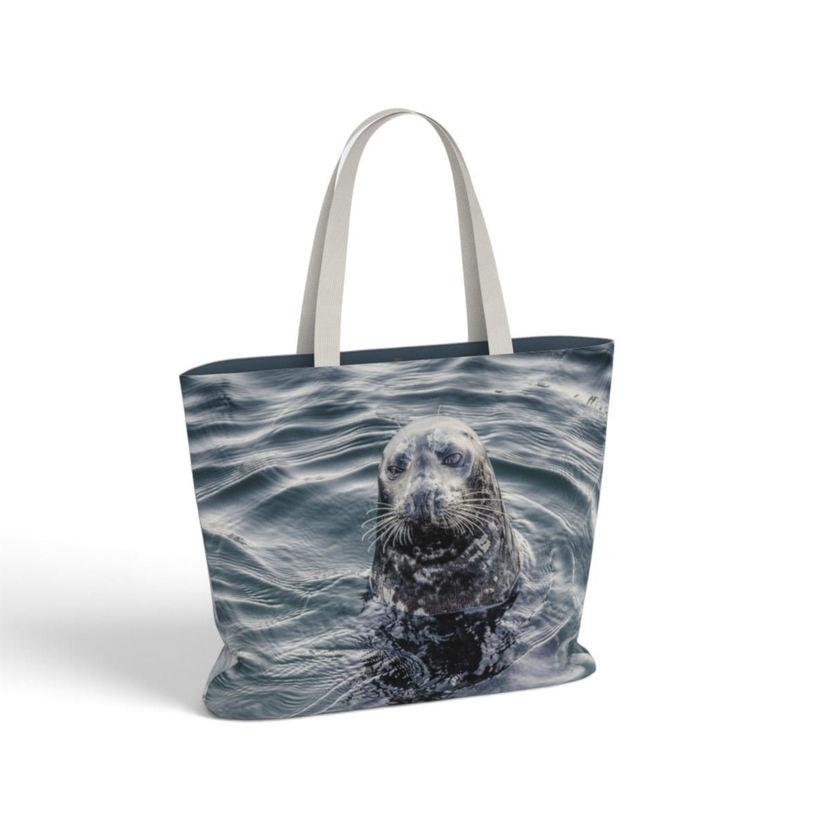 A tote bag featuring a photographic print of a seal swimming in blue-gray water, with light gray fabric handles, shown on a plain white background.