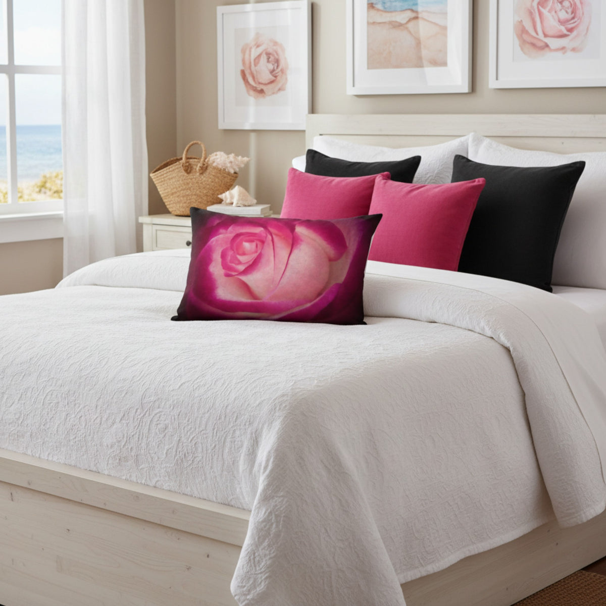A bedroom scene with a made bed in soft neutral tones, featuring decorative throw pillows including a prominent rectangular pillow with a pink rose print, alongside solid black and hot pink pillows.