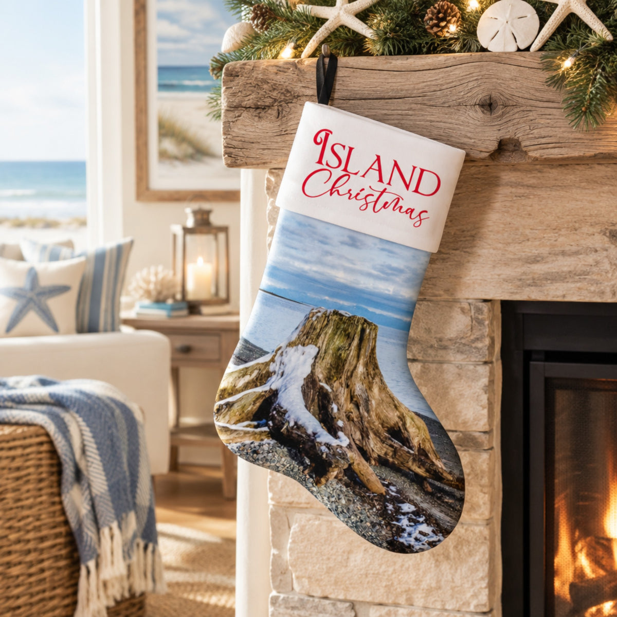 A Christmas stocking with a printed coastal landscape and the words “Island Christmas” in red script, hanging from a rustic wooden mantel in a cozy living room with a fireplace and beach decor in the background.