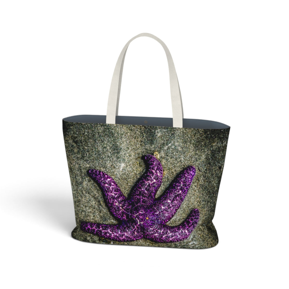 A tote bag featuring a textured dark gray and green stone-like print with a large purple starfish design on the front, finished with white shoulder straps.