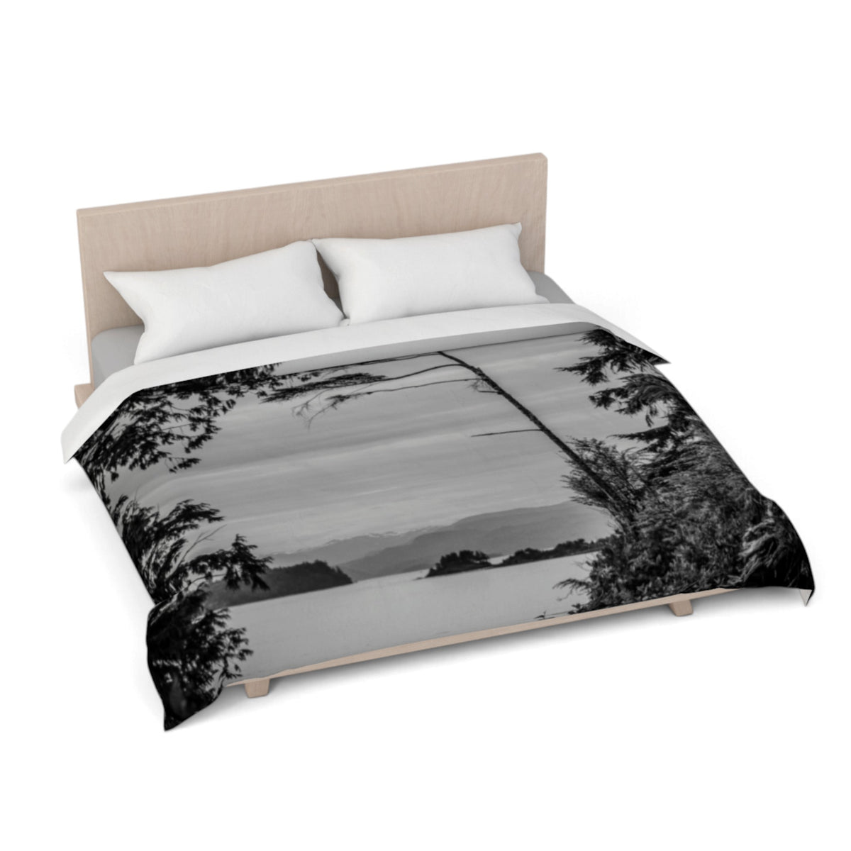 A bed dressed with a duvet cover featuring a black and white landscape photograph of a lake and trees, styled with a light wood headboard and white pillows on a white background.