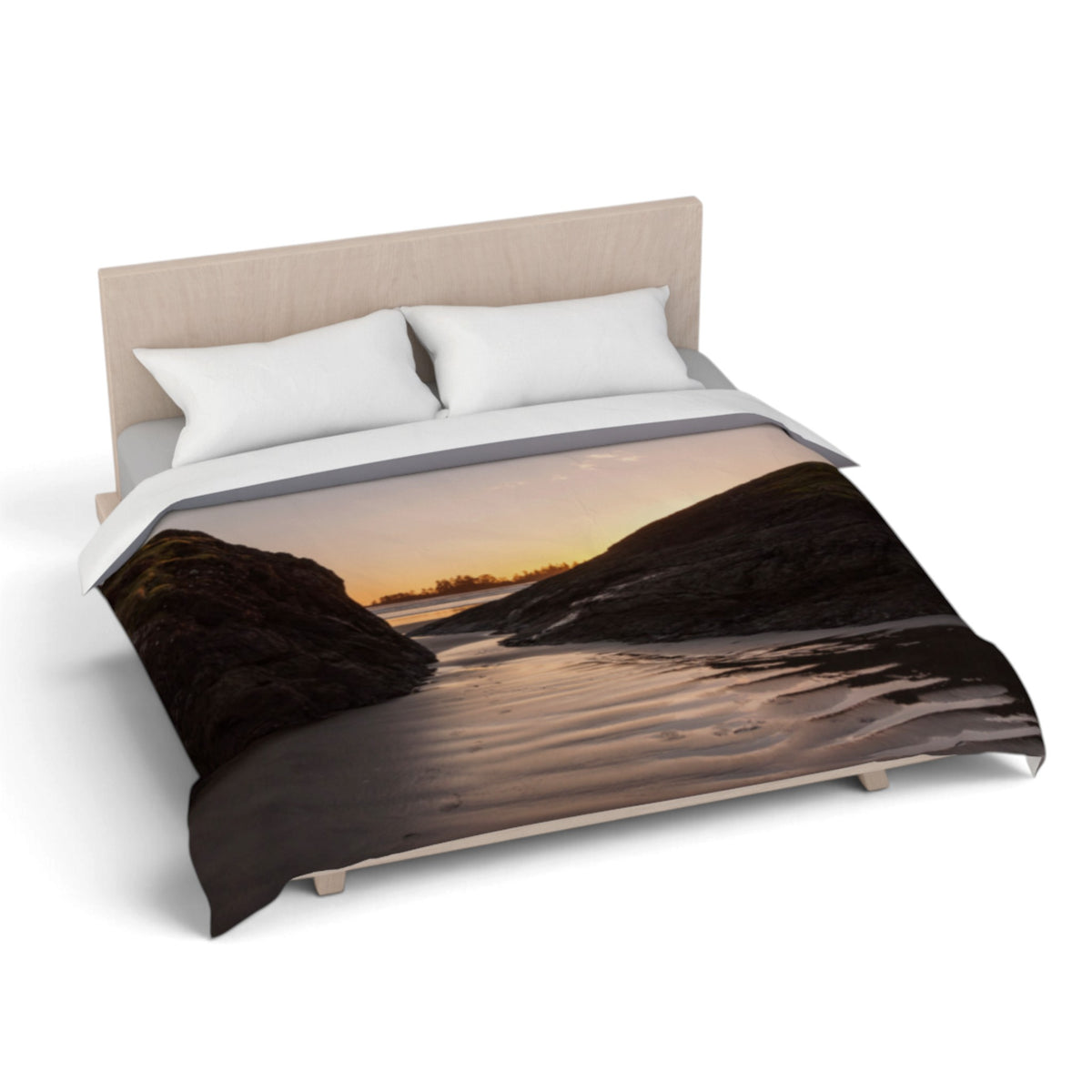 A bed dressed with a duvet cover featuring a scenic landscape print of a rocky shoreline at sunset, styled with two white pillows and a light wood headboard on a white background.