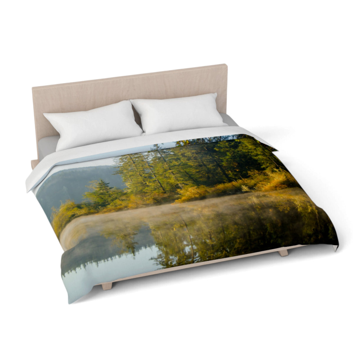 A bed dressed with a duvet cover featuring a scenic forest lake reflection print, styled with two white pillows and a light wood headboard on a white background.
