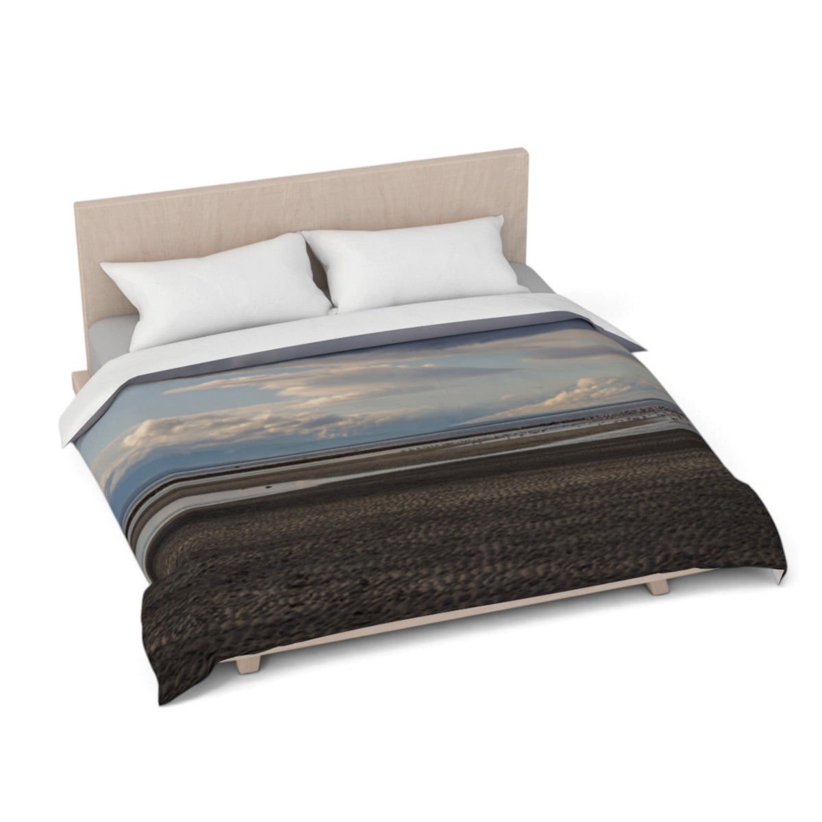 A bed dressed with a duvet cover featuring a scenic landscape print of a dark beach or field under a cloudy blue sky, styled with a light wood headboard and two white pillows on a white background.