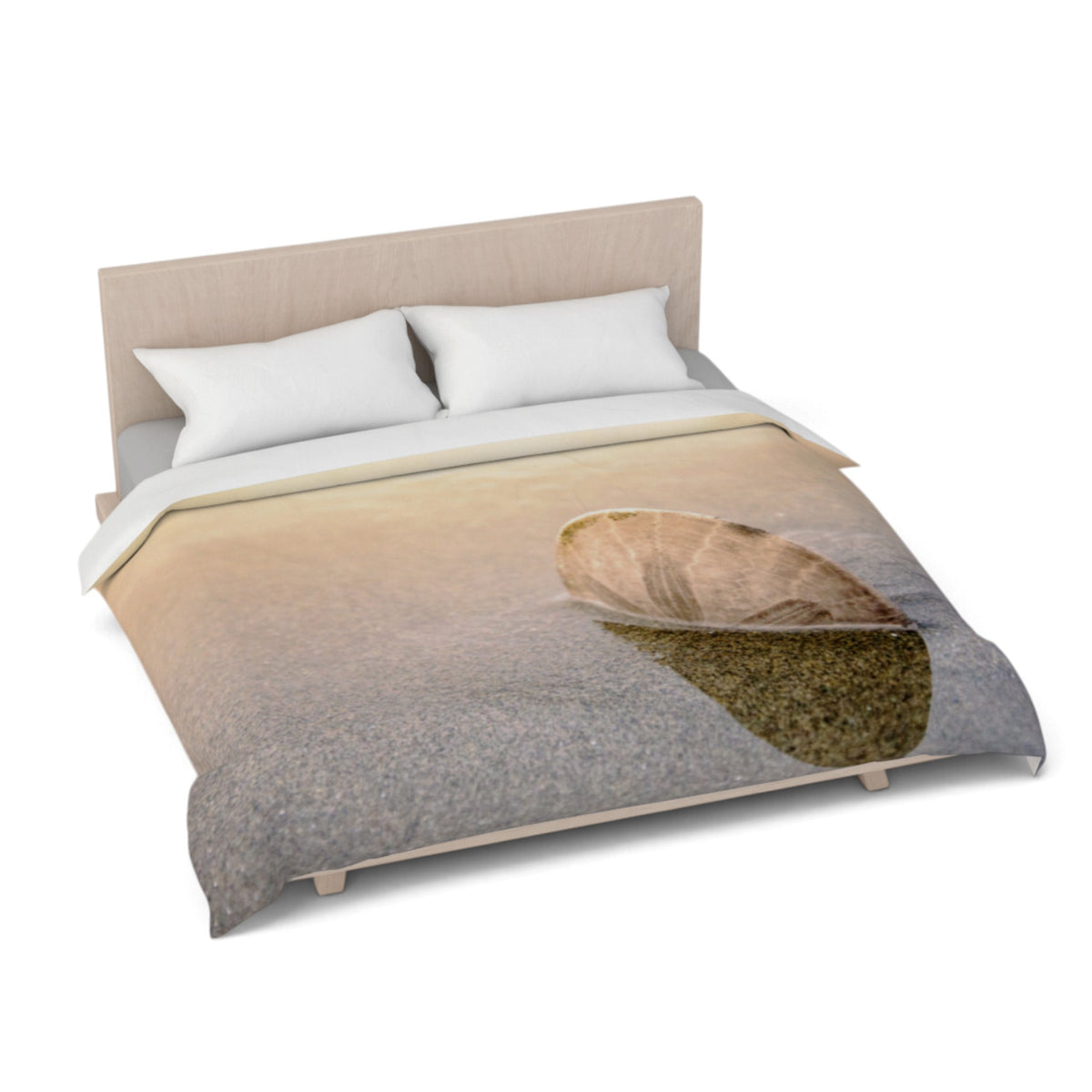 A bed dressed with a duvet cover featuring a printed beach scene with a large shell on sand, shown on a white studio background with a light wood headboard and two white pillows.
