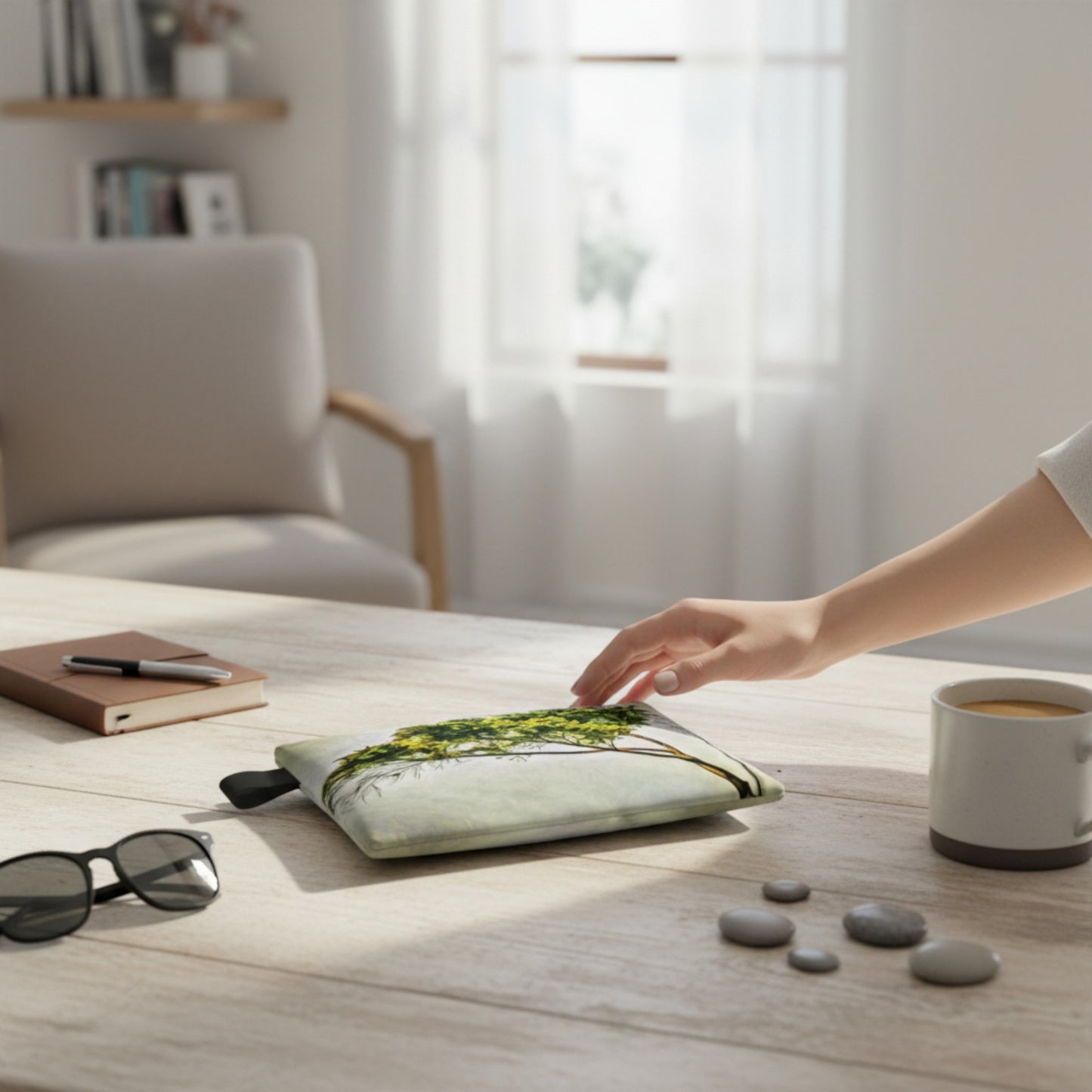Person placing a small plant on a desk with a cup of coffee, sunglasses, and a notebook.