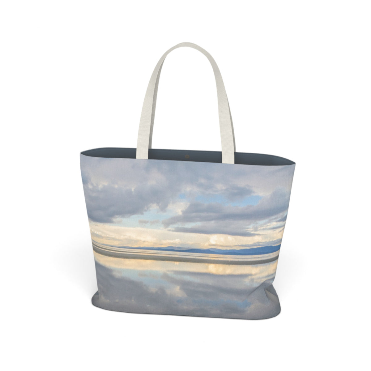 A tote bag featuring a photographic print of a cloudy sky reflected in calm water, with light beige shoulder straps, shown on a plain white background.