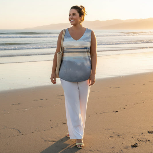 Woman standing on a beach wearing a sleeveless top and white pants.