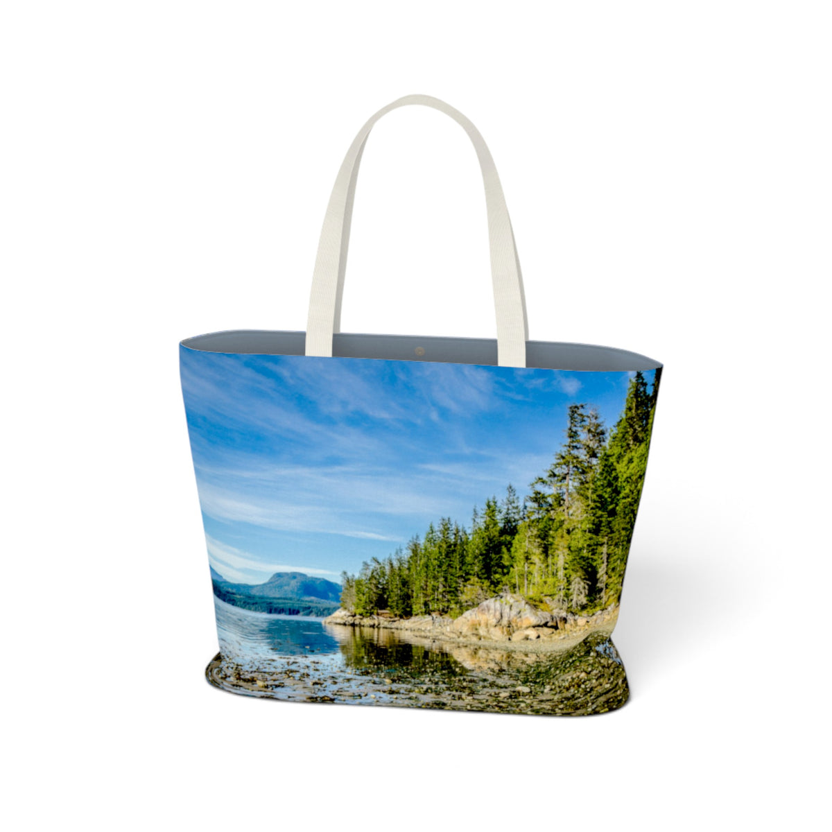 A tote bag with a scenic landscape print of a lake, forest, and mountains under a blue sky, featuring off-white fabric handles, shown on a white background.