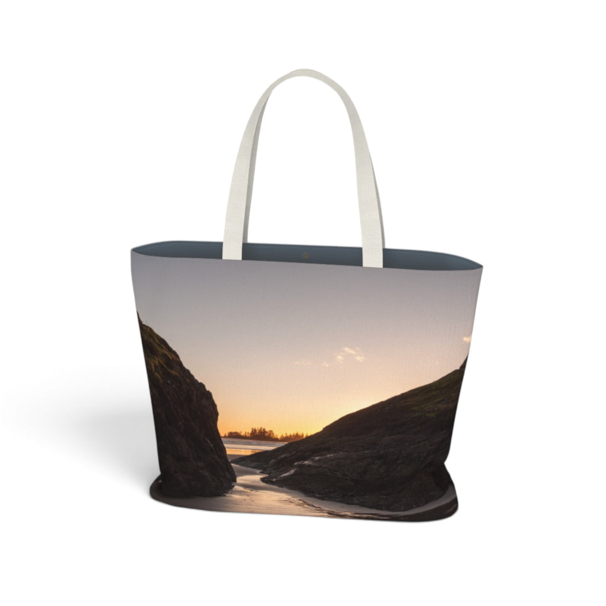 A tote bag with a printed landscape photograph of a rocky shoreline at sunset, featuring white shoulder straps, shown on a plain white background.