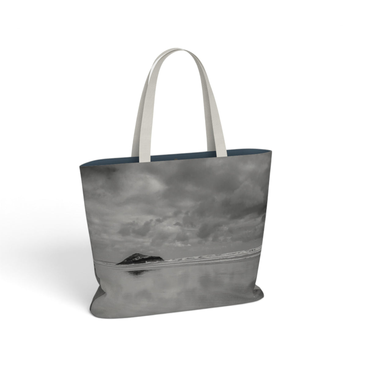 A tote bag featuring a black and white landscape photograph of a rocky sea island, with contrasting off-white shoulder straps, shown on a plain white background.